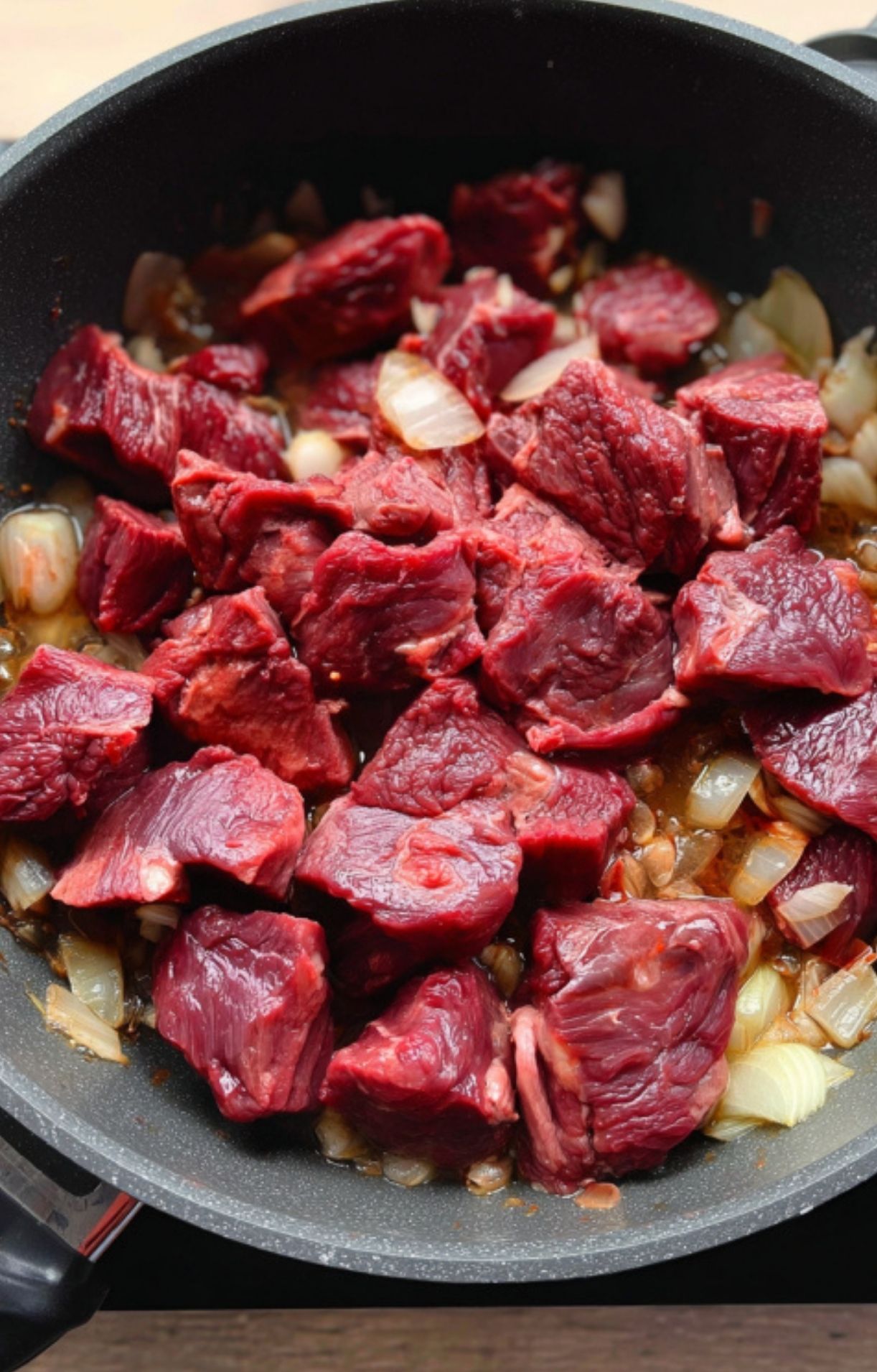 Chunks of raw beef browning with onions in a skillet, the first step for making traditional Hungarian goulash. Shows the importance of building flavor for hearty stew recipes.