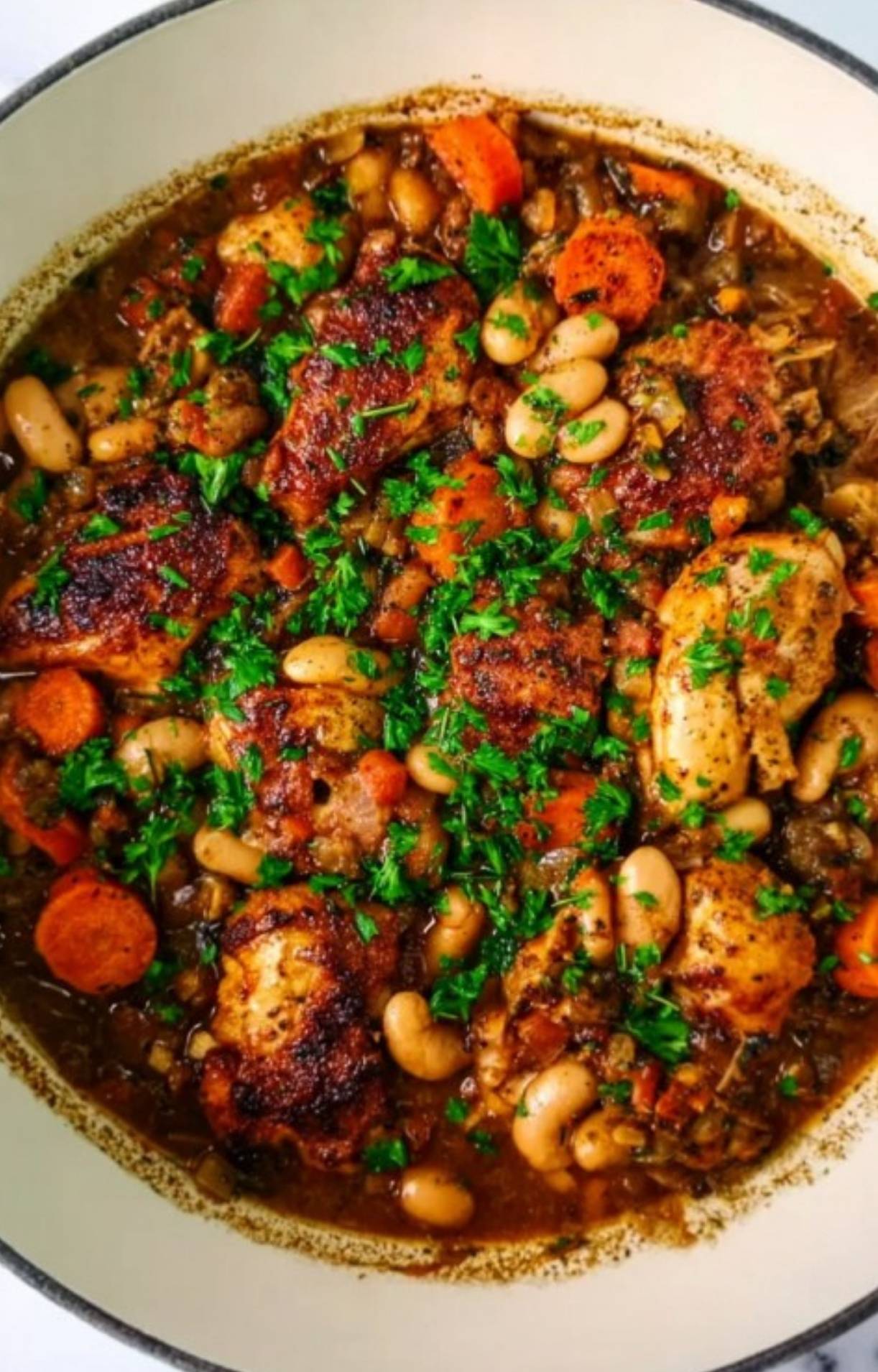 Baked Chicken Cassoulet in a Dutch oven with white beans, carrots, and parsley, perfect for a hearty family dinner.