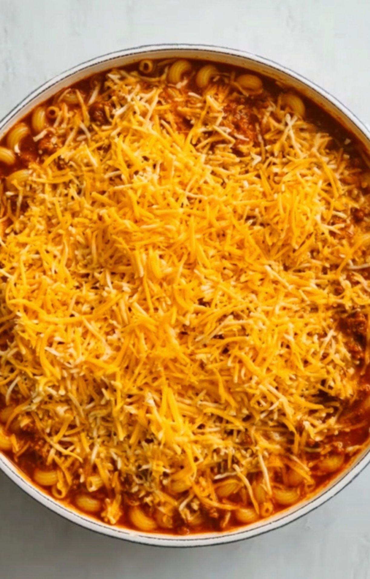 Large pot filled with uncooked shredded cheddar cheese, beef, and macaroni ready to bake. Easy family casserole loaded with cheese for busy nights.