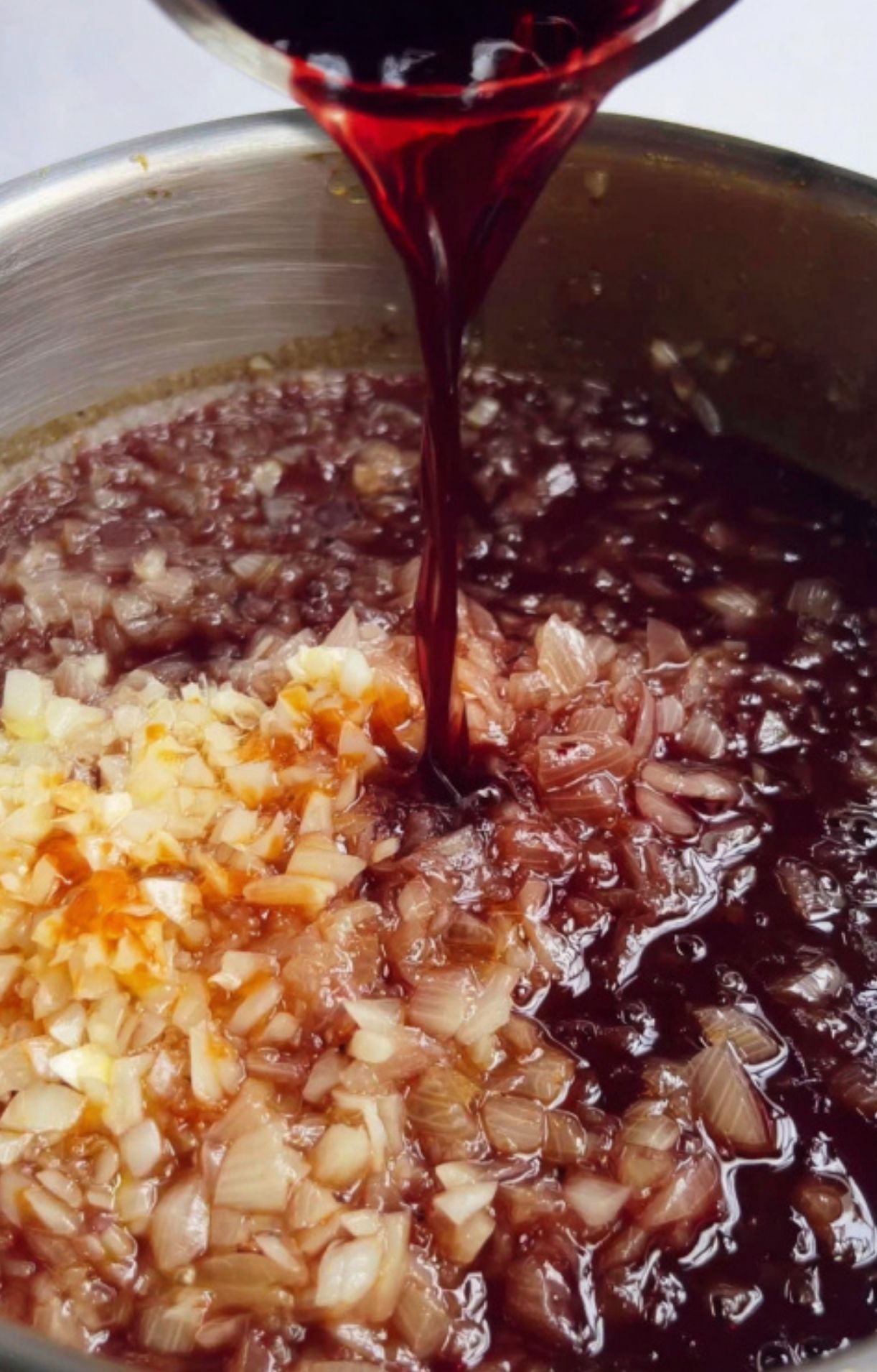 Red wine being poured over sautéed onions and garlic for extra depth in homemade beef goulash. Ideal for cozy winter recipes and German comfort meals.