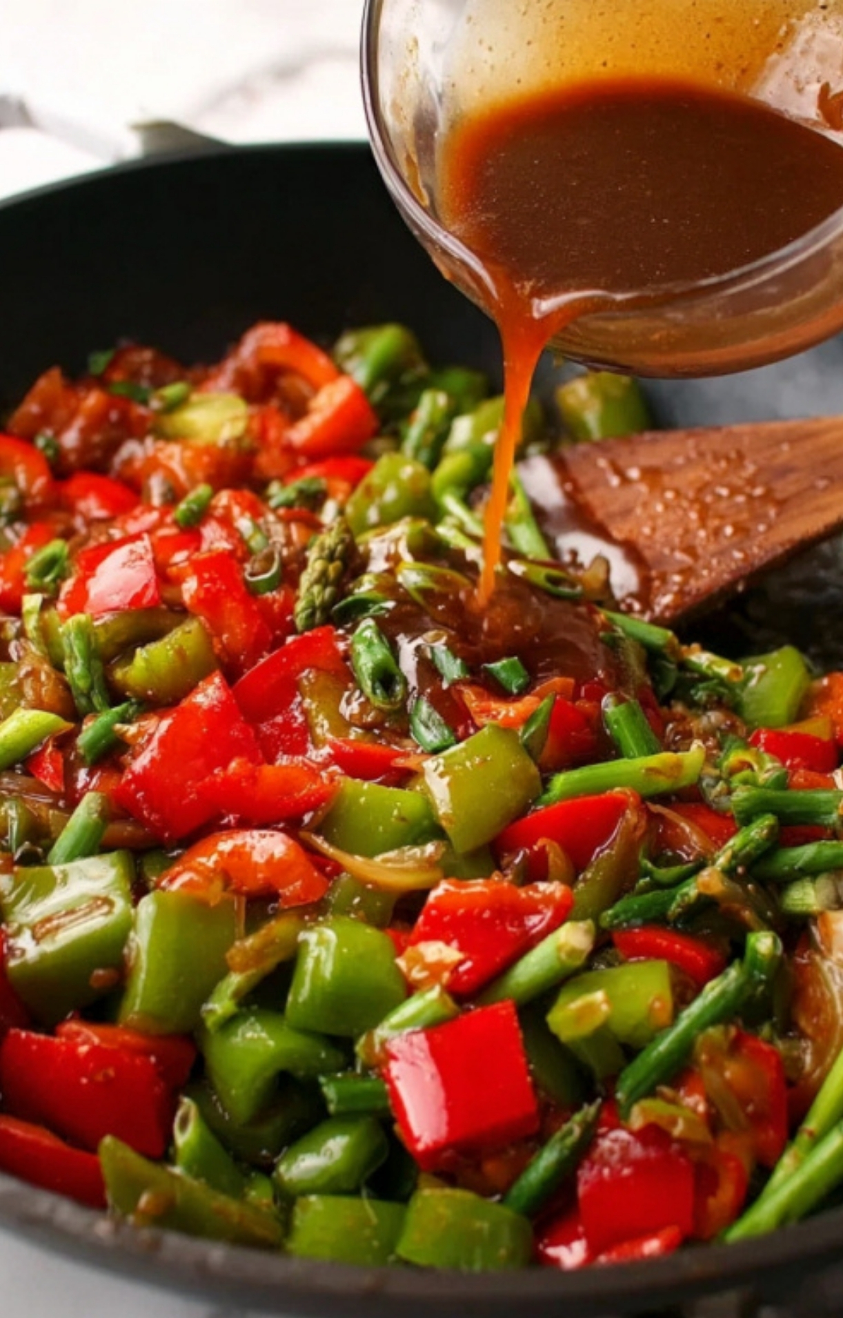 Pouring homemade pepper steak sauce over sautéed bell peppers and beef for rich flavor.
