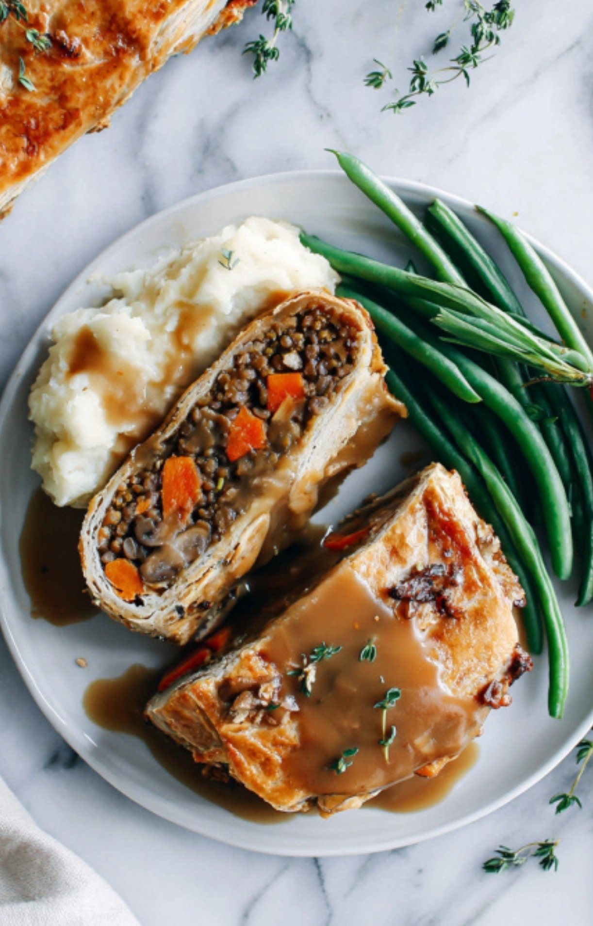 Thick slices of vegan beef wellington topped with rich gravy, served with fluffy mashed potatoes and crisp green beans on a holiday table.