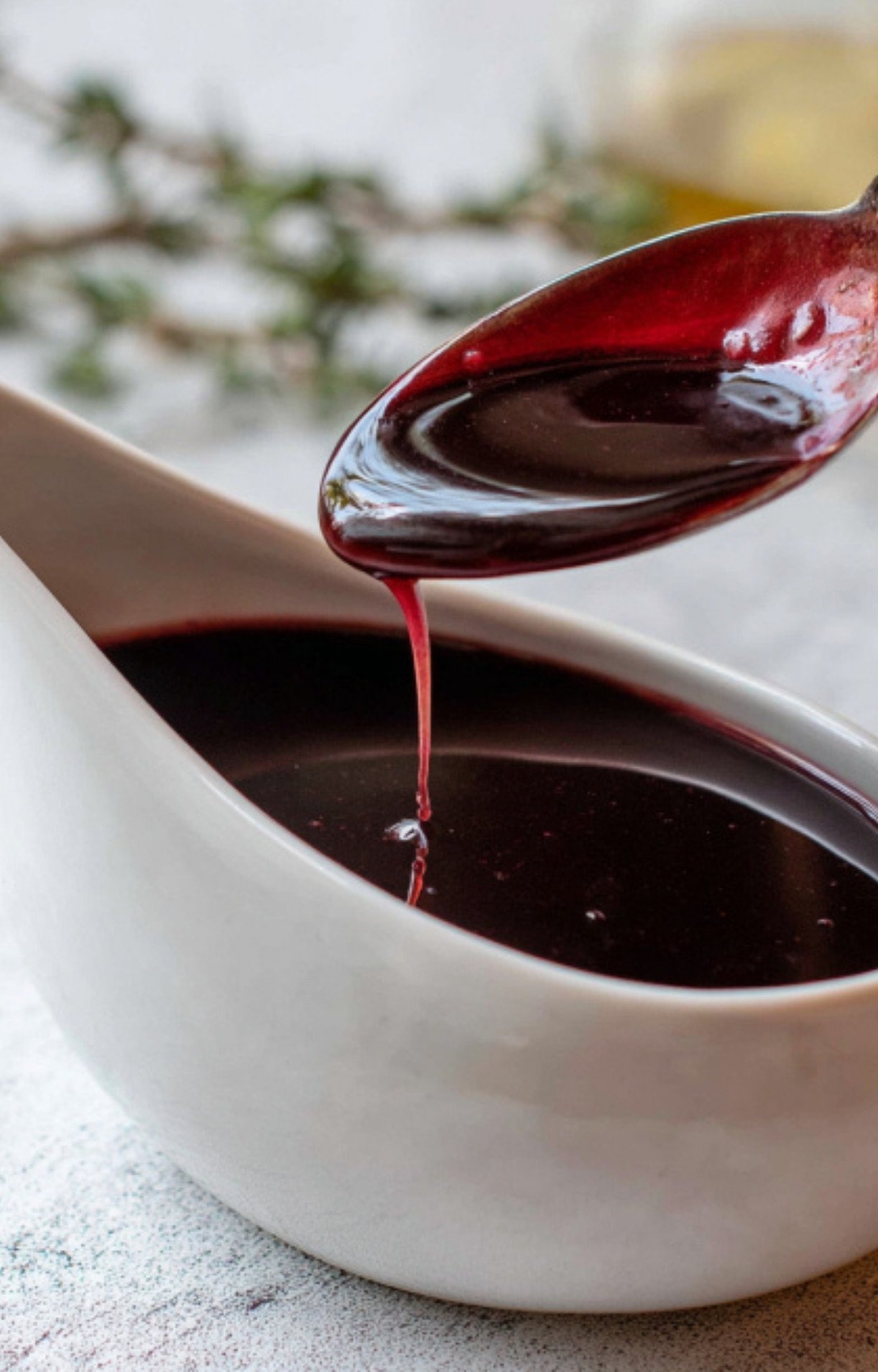 Spoon drizzling glossy homemade red wine sauce from a gravy boat, ideal for steak, beef wellington, or festive dinners.