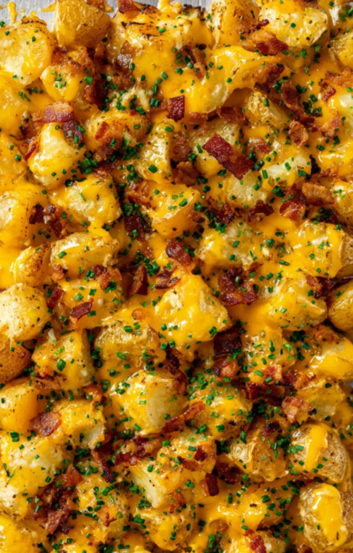 Sheet pan of finished cheesy bacon ranch potatoes with melted cheddar, crispy bacon, and fresh chives ready to serve.