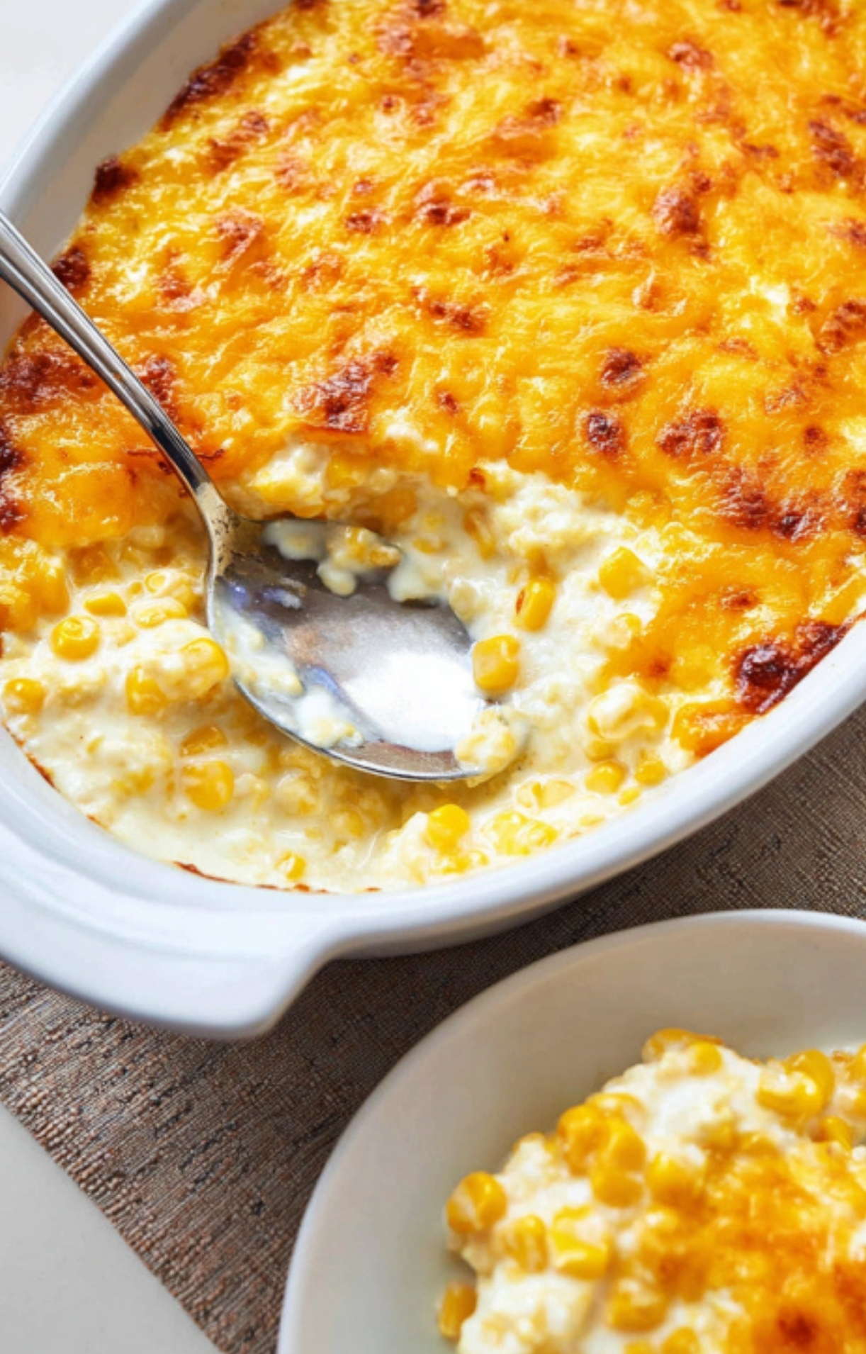 Freshly baked cream cheese corn casserole with a golden cheese top, a spoon scooping out the creamy filling for serving.