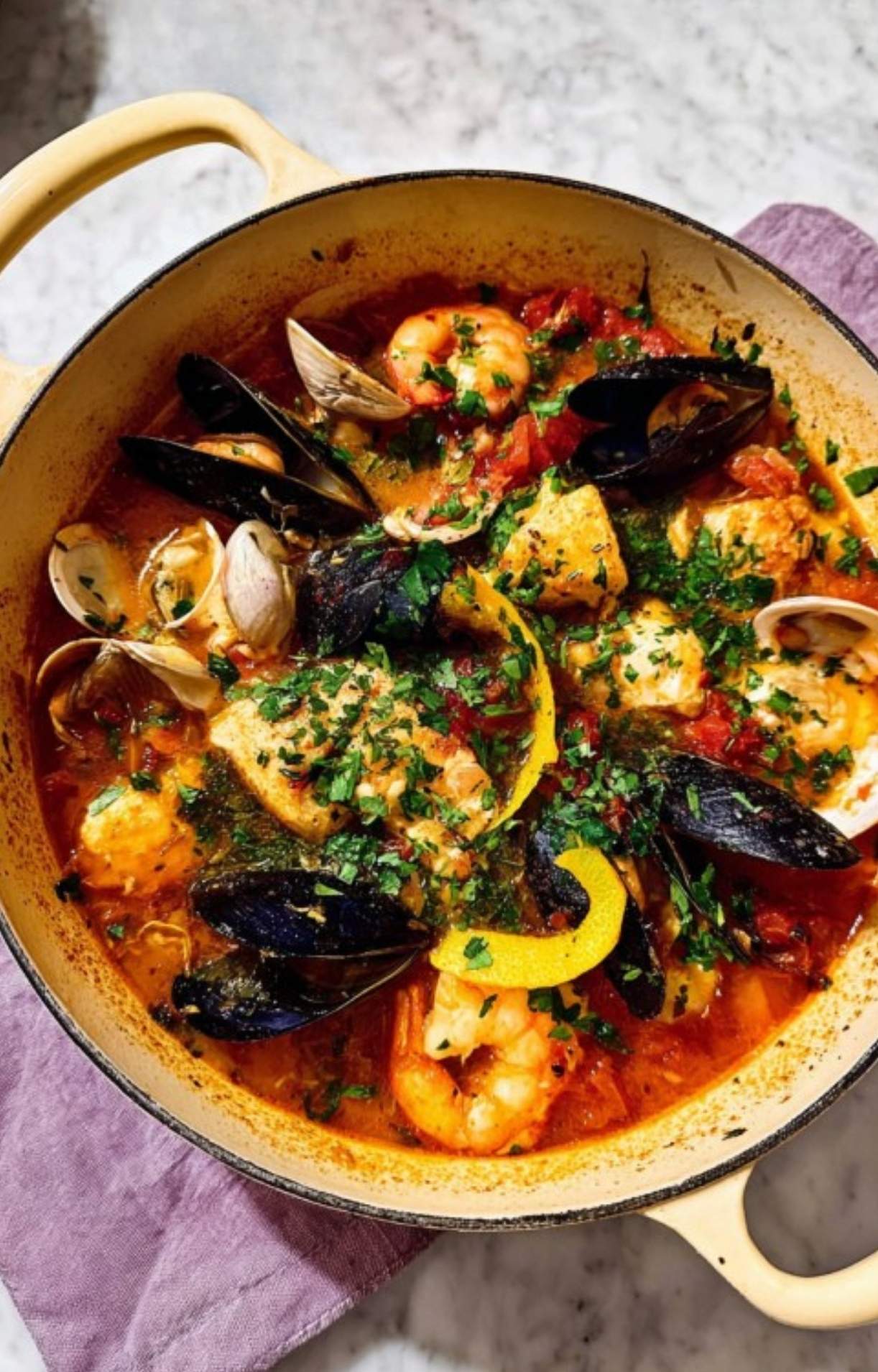 Bright and hearty bouillabaisse seafood stew in a cream pot featuring mussels, clams, white fish, and shrimp in golden tomato-saffron broth. Best French fish stew for winter gatherings and special occasions.
