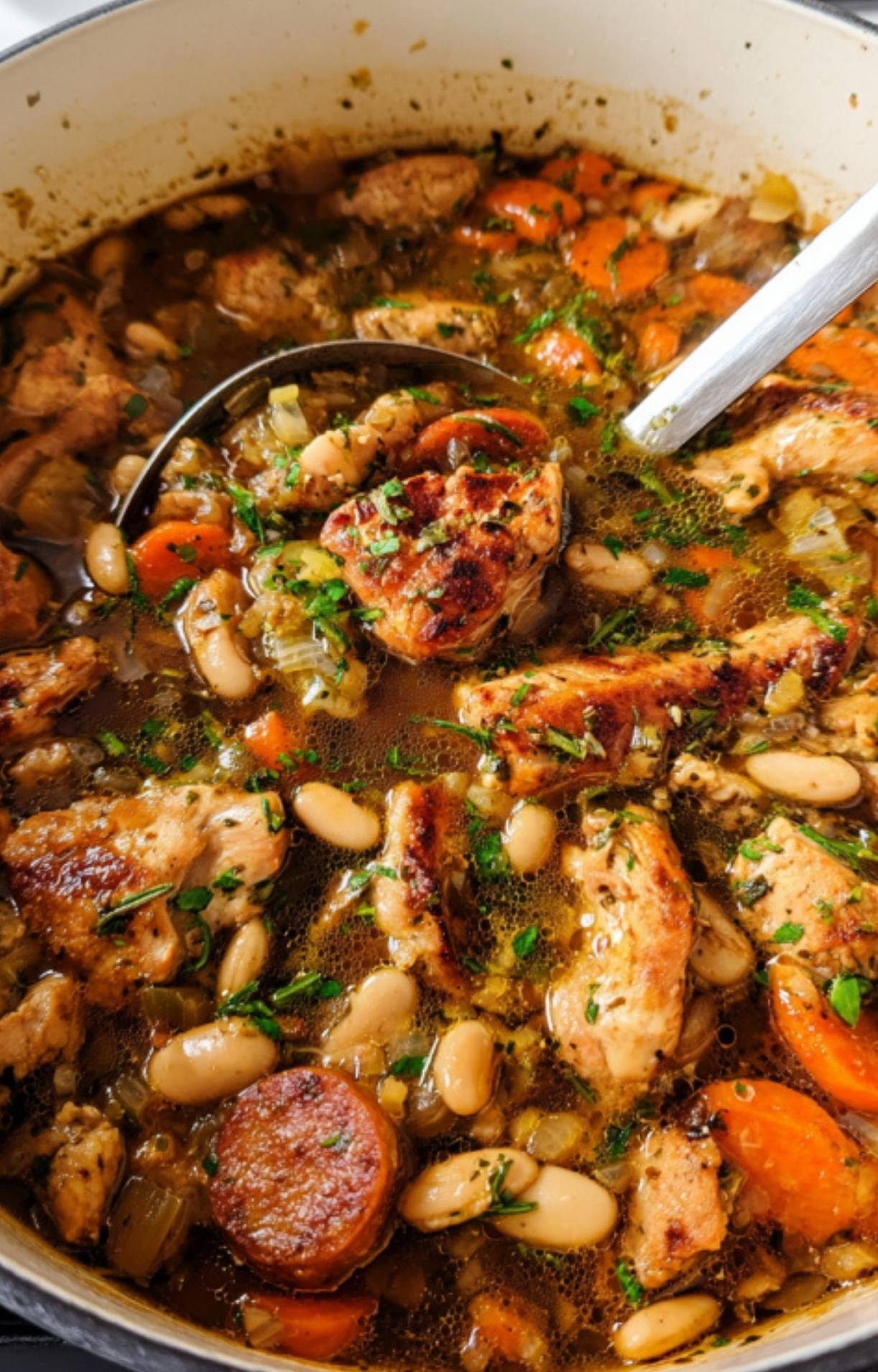 Dutch oven filled with Chicken Cassoulet, showing golden chicken pieces, sliced sausage, carrots, white beans, and herbs in a savory broth.