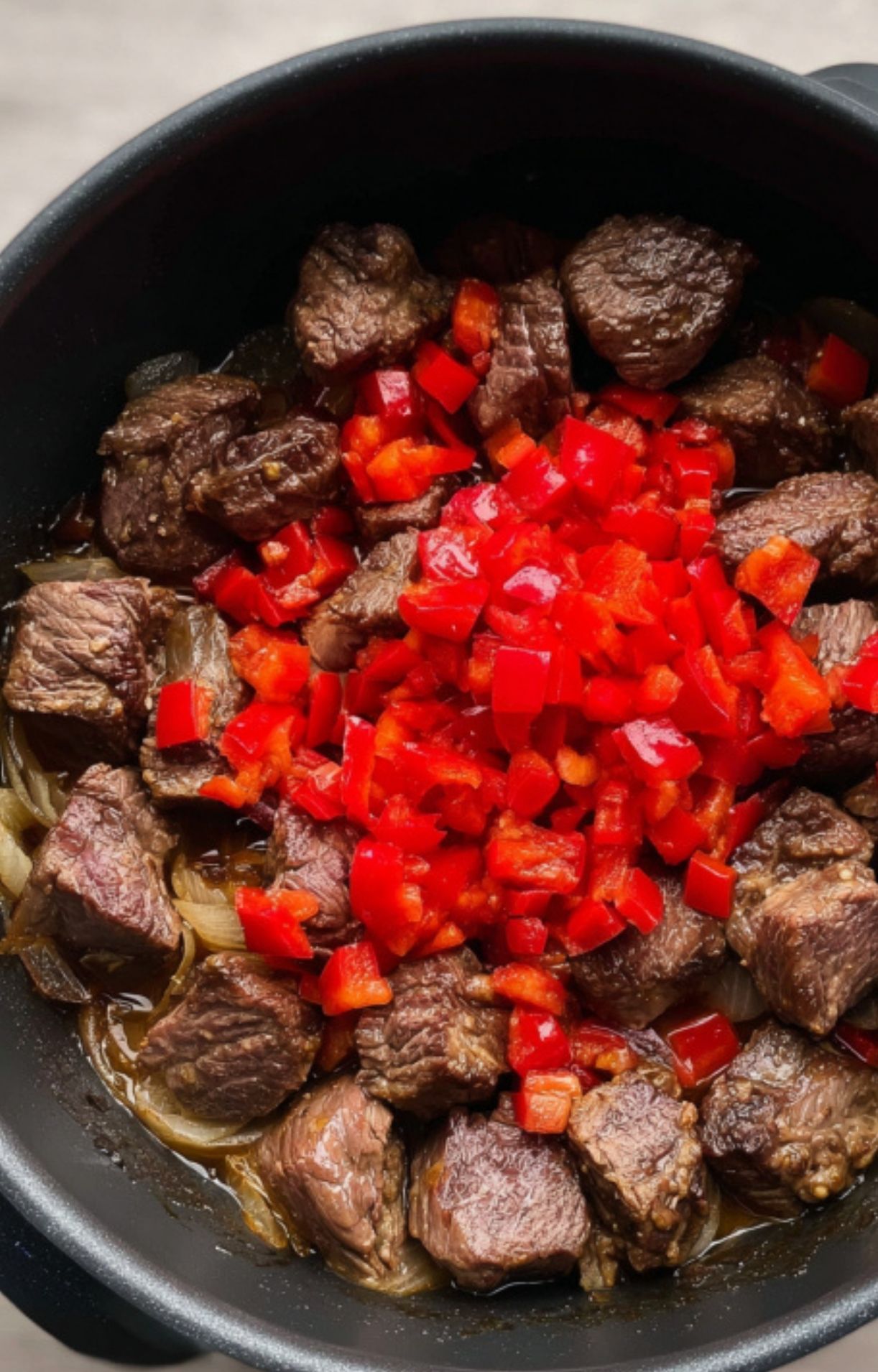 Chunks of browned beef with chopped red bell peppers in a pot, showing the process of building flavor for authentic Hungarian goulash.