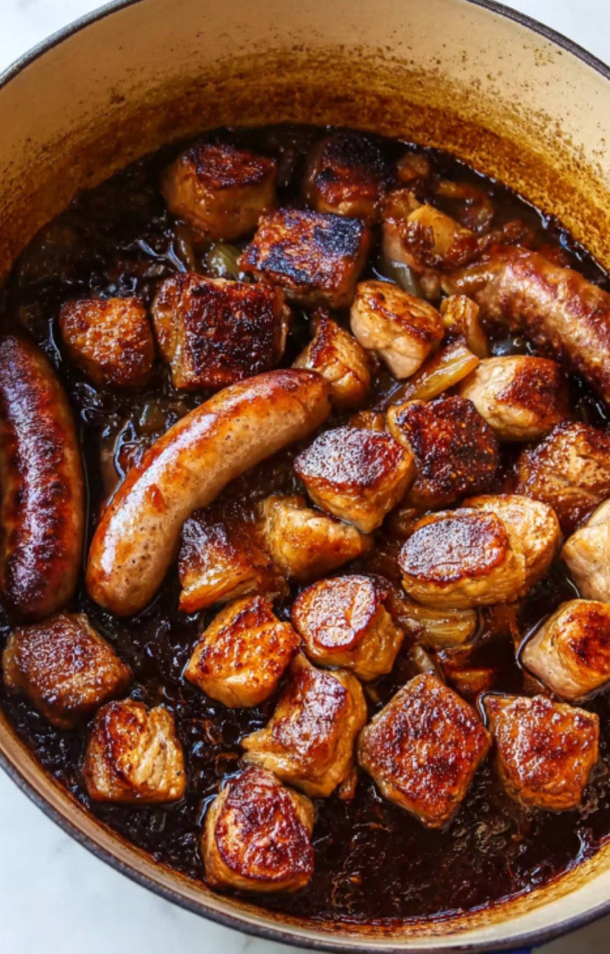 Chunks of pork shoulder and sausage browning in a Dutch oven, an essential step for a classic cassolette recipe, bringing big flavor to this French comfort food favorite.