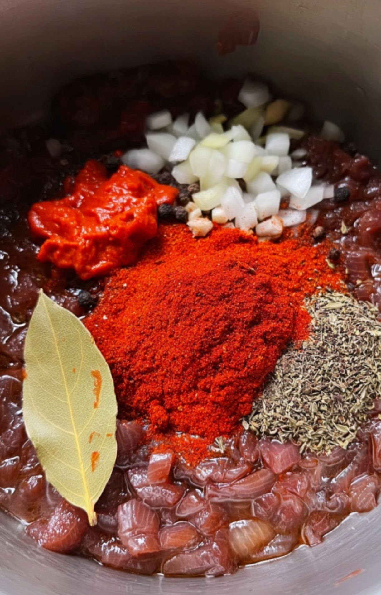 A closeup of chopped onions, paprika, tomato paste, and bay leaf in a pot, ready to create a savory and aromatic goulash base. Best for easy stew recipes and classic German dinners.