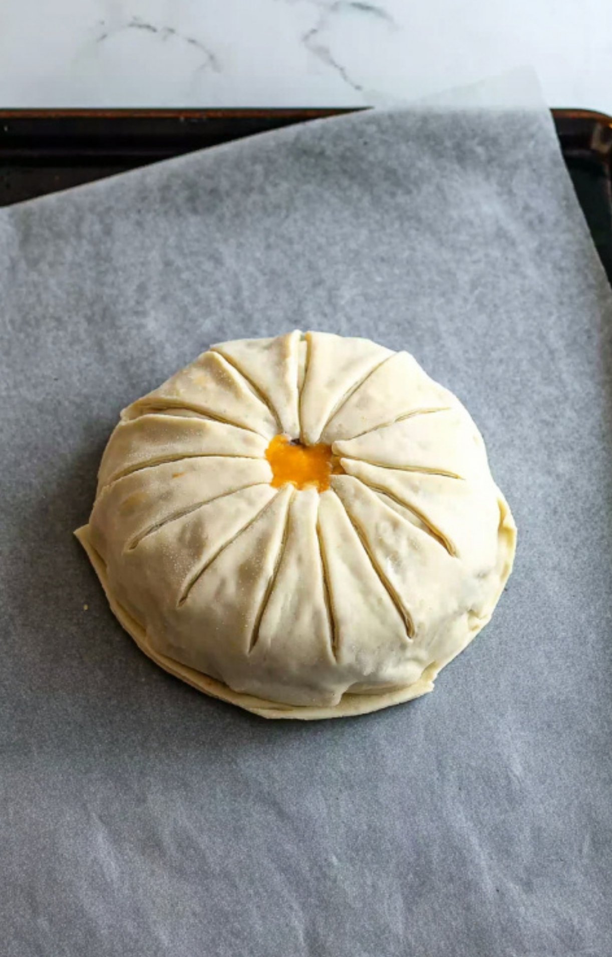 Unbaked Beef Wellington covered in puff pastry with decorative slits and an egg wash center, sitting on parchment paper. Perfect step before baking for a golden, flaky crust that’s ideal for holiday entertaining and special dinners.