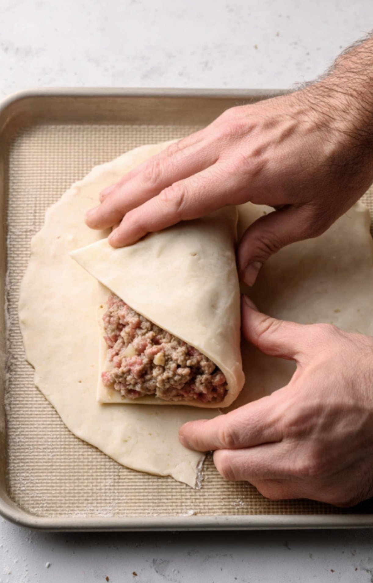 Hands folding puff pastry around a savory ground beef filling, showing easy steps for making beef Wellington at home.