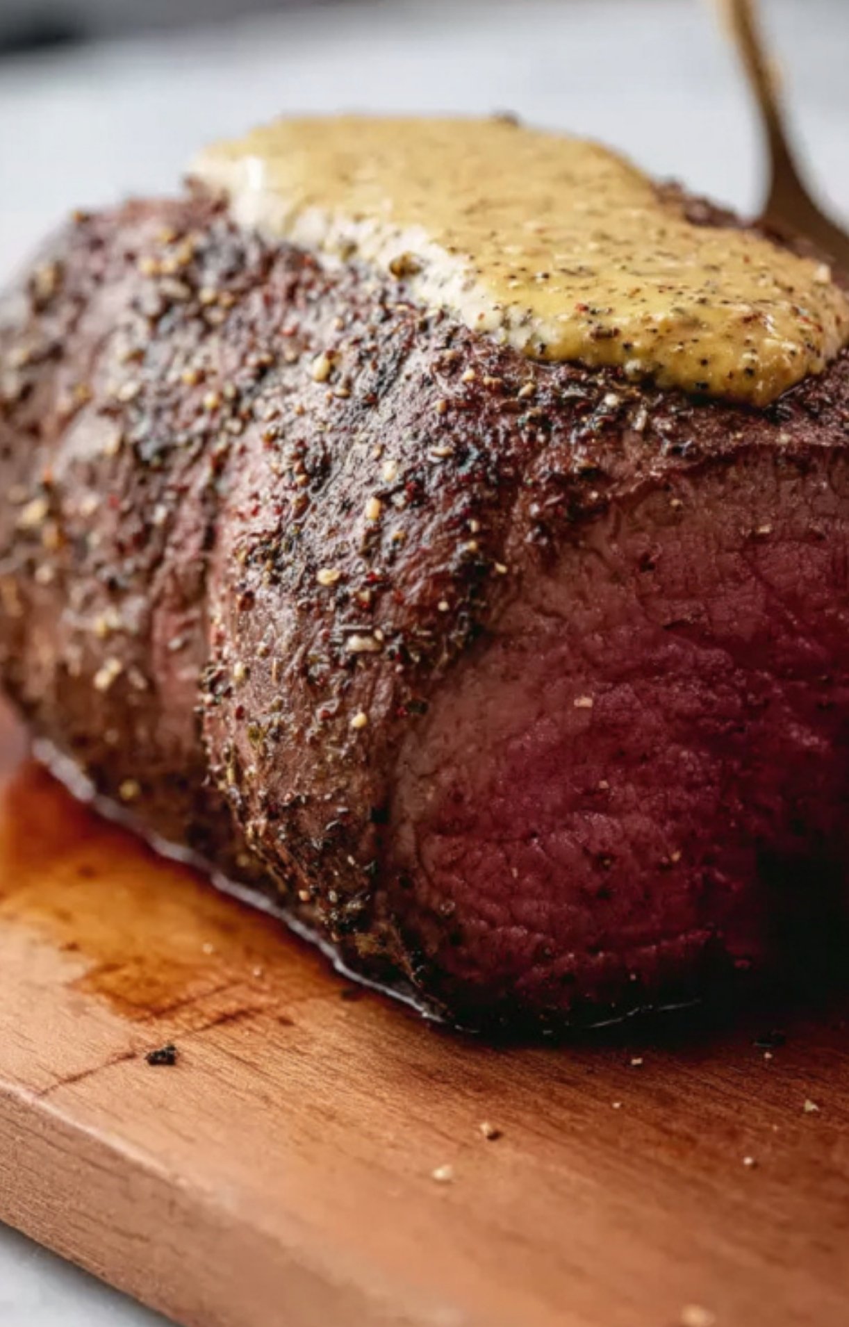 Beef tenderloin coated with cracked pepper and salt, topped with a layer of mustard, ready to be wrapped in pastry for classic beef wellington.