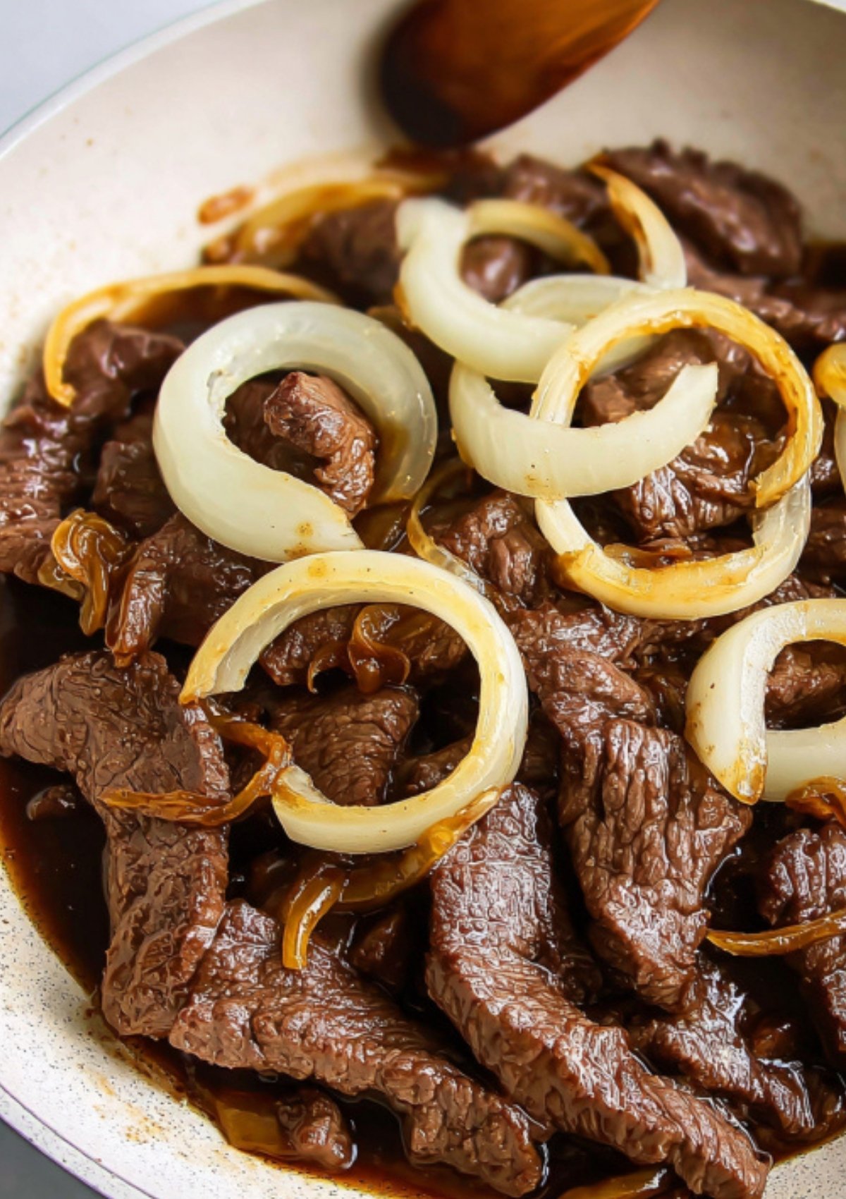 Tender Filipino beef steak layered with onion rings and savory sauce on a serving plate.