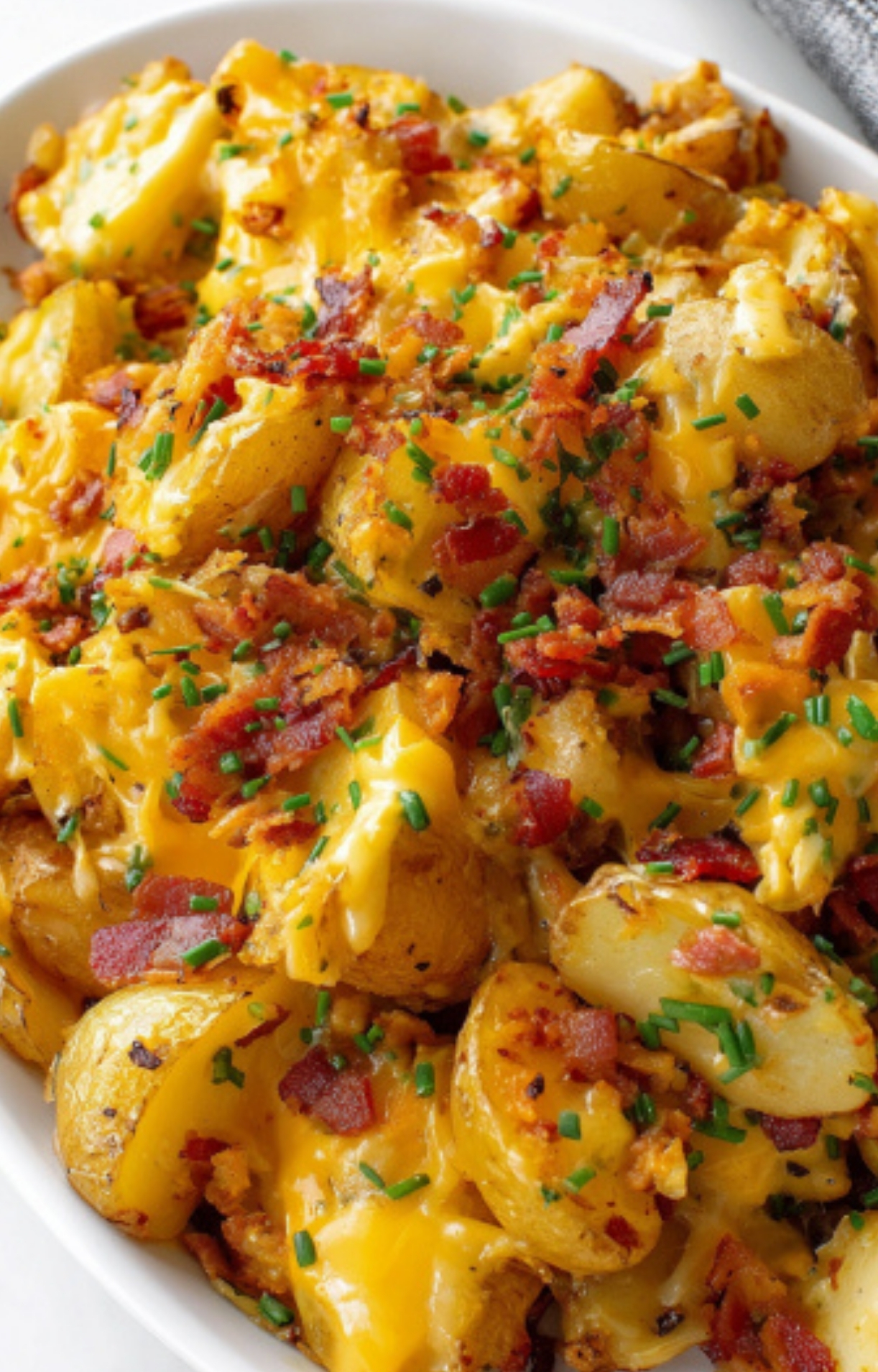 Baking dish filled with cheesy bacon ranch potatoes, featuring roasted potatoes, melted cheddar, smoky bacon, and fresh chives, perfect for family dinners or potlucks.
