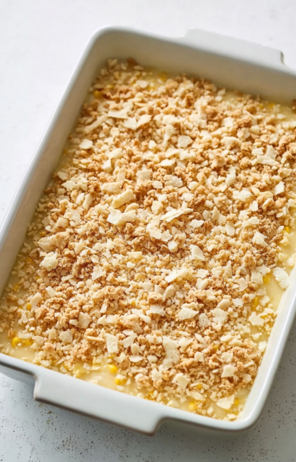 Casserole dish filled with scalloped corn and a layer of crushed crackers, ready for the oven, classic holiday recipe.
