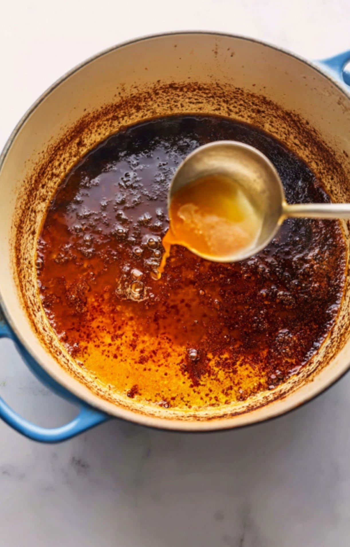 Ladle of rich broth in a Dutch oven after browning meats for cassolette recipe, the secret to a flavorful French stew perfect for holidays and family meals.