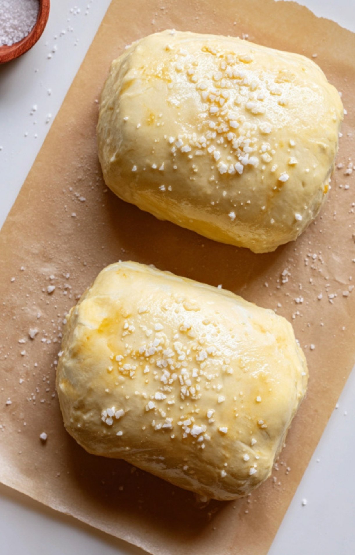 Two beef Wellington parcels brushed with egg wash and sprinkled with flaky sea salt, ready to bake for a crispy, golden crust.