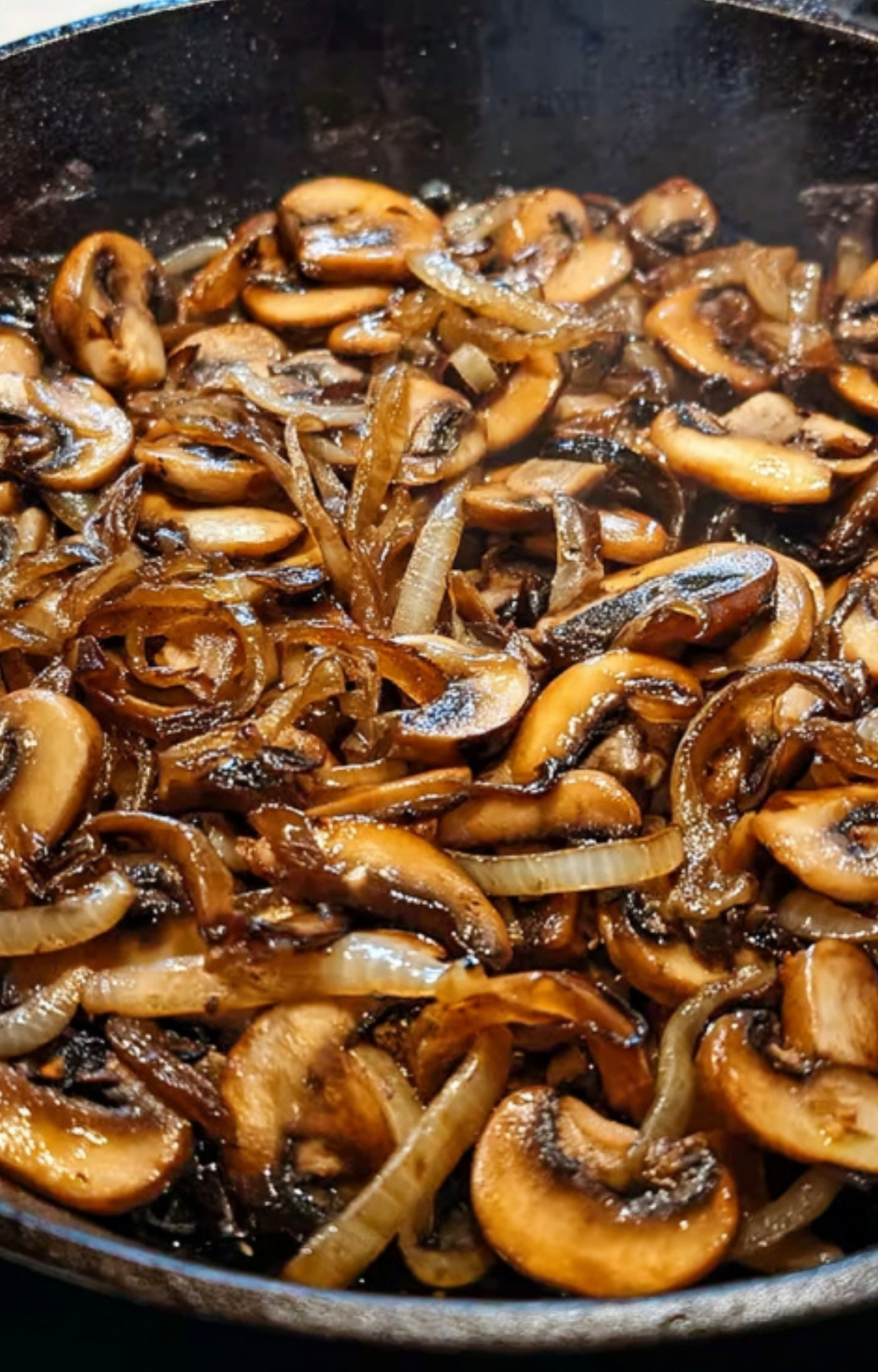 Golden sautéed mushrooms and onions in a skillet, cooked for classic homemade Salisbury steak.