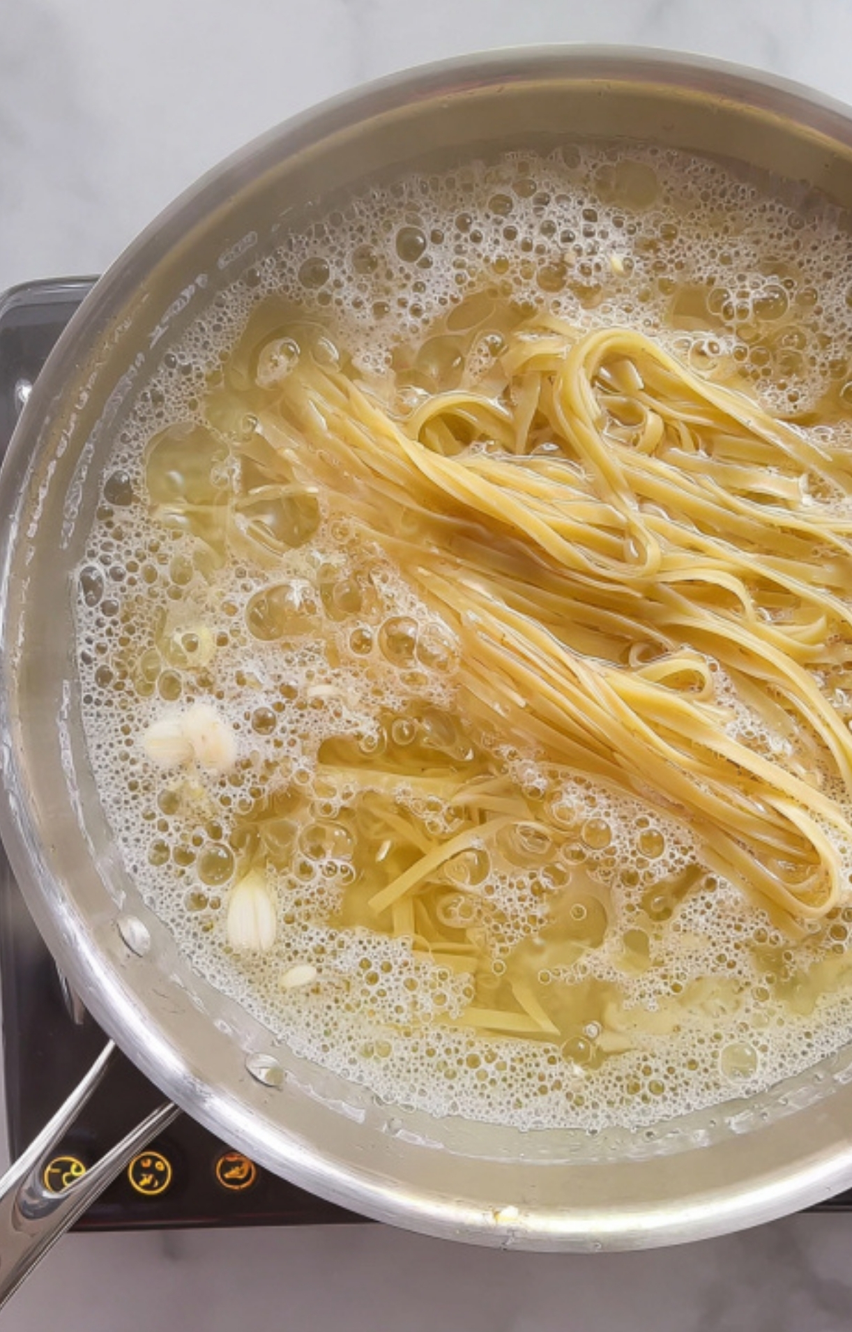 Fettuccine noodles boiling in a pot with garlic cloves, prepping for a fast and cozy vegetarian dinner.
