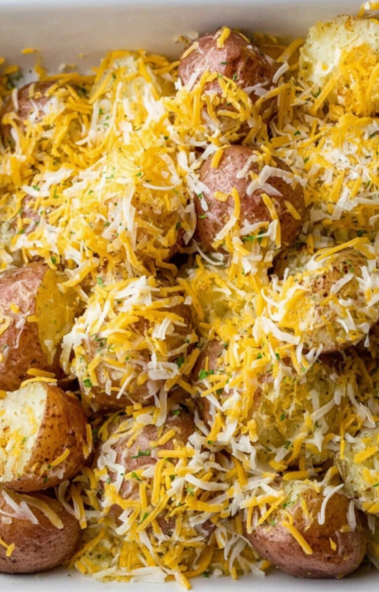 Baby red potatoes in a casserole dish smothered with a generous layer of shredded cheese, ready for baking.