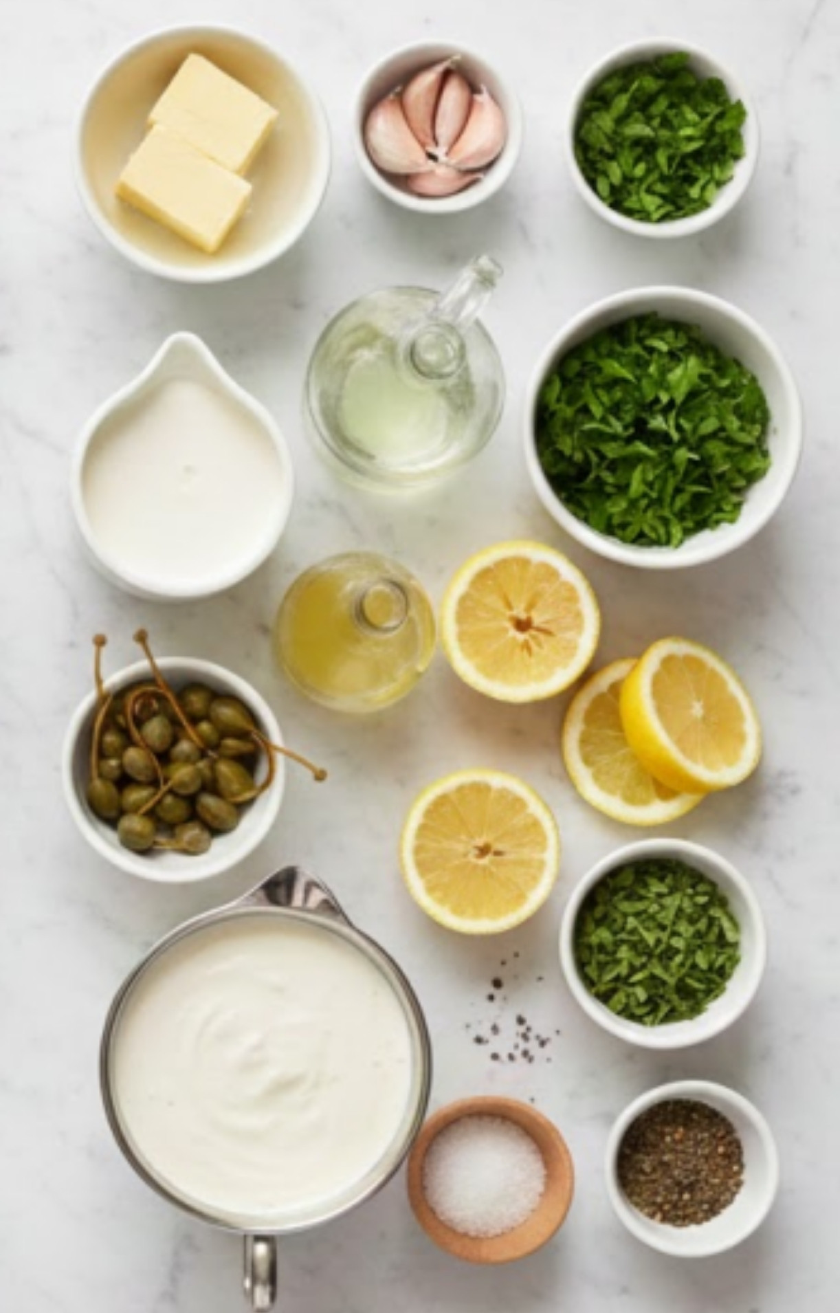 A flat lay of ingredients including butter, garlic cloves, chopped parsley, lemon halves, capers, cream, and seasonings.