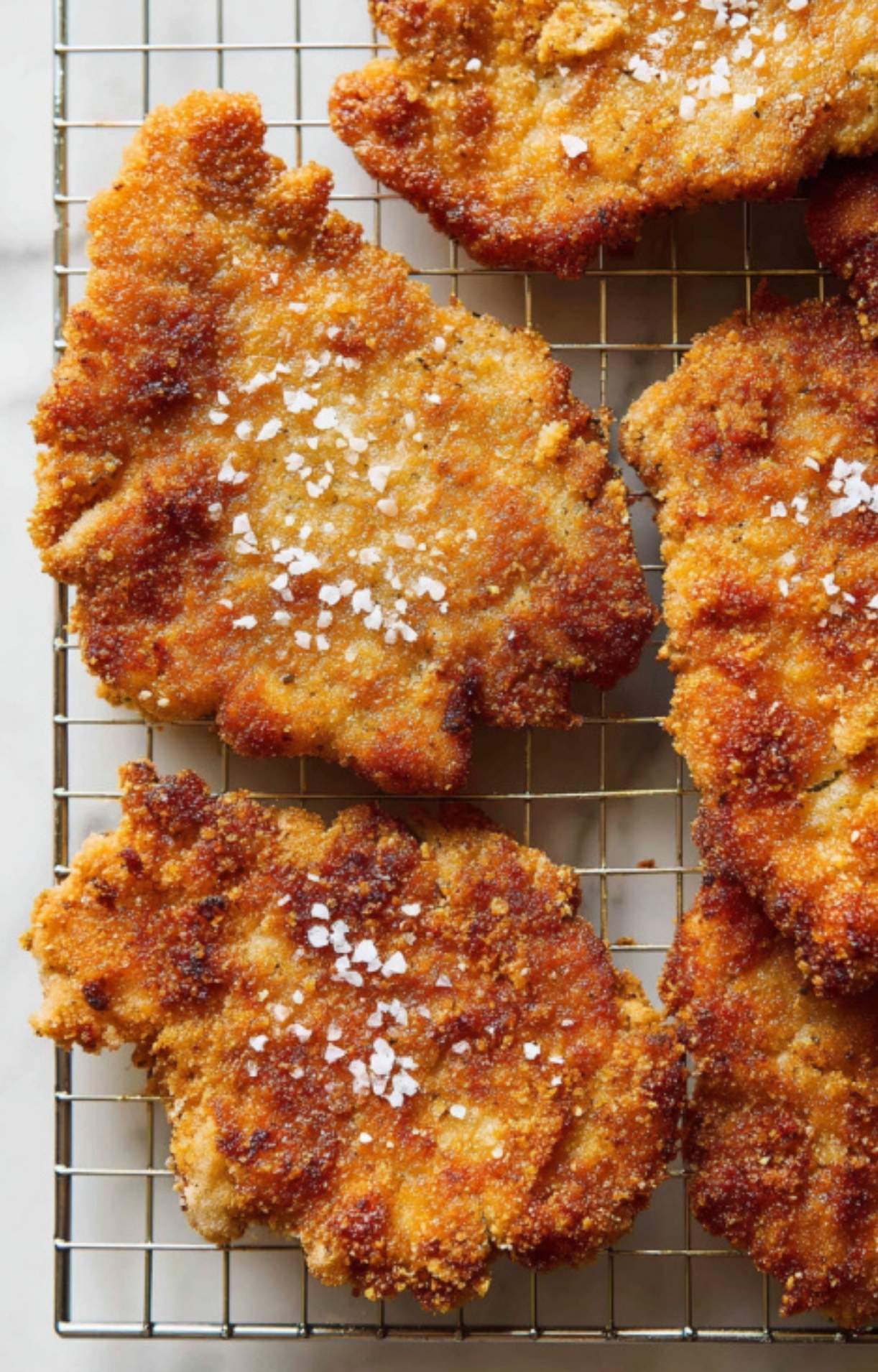 Golden brown veal cutlets cooling on a rack with flaky salt, perfect for classic veal scallopini Milanese.