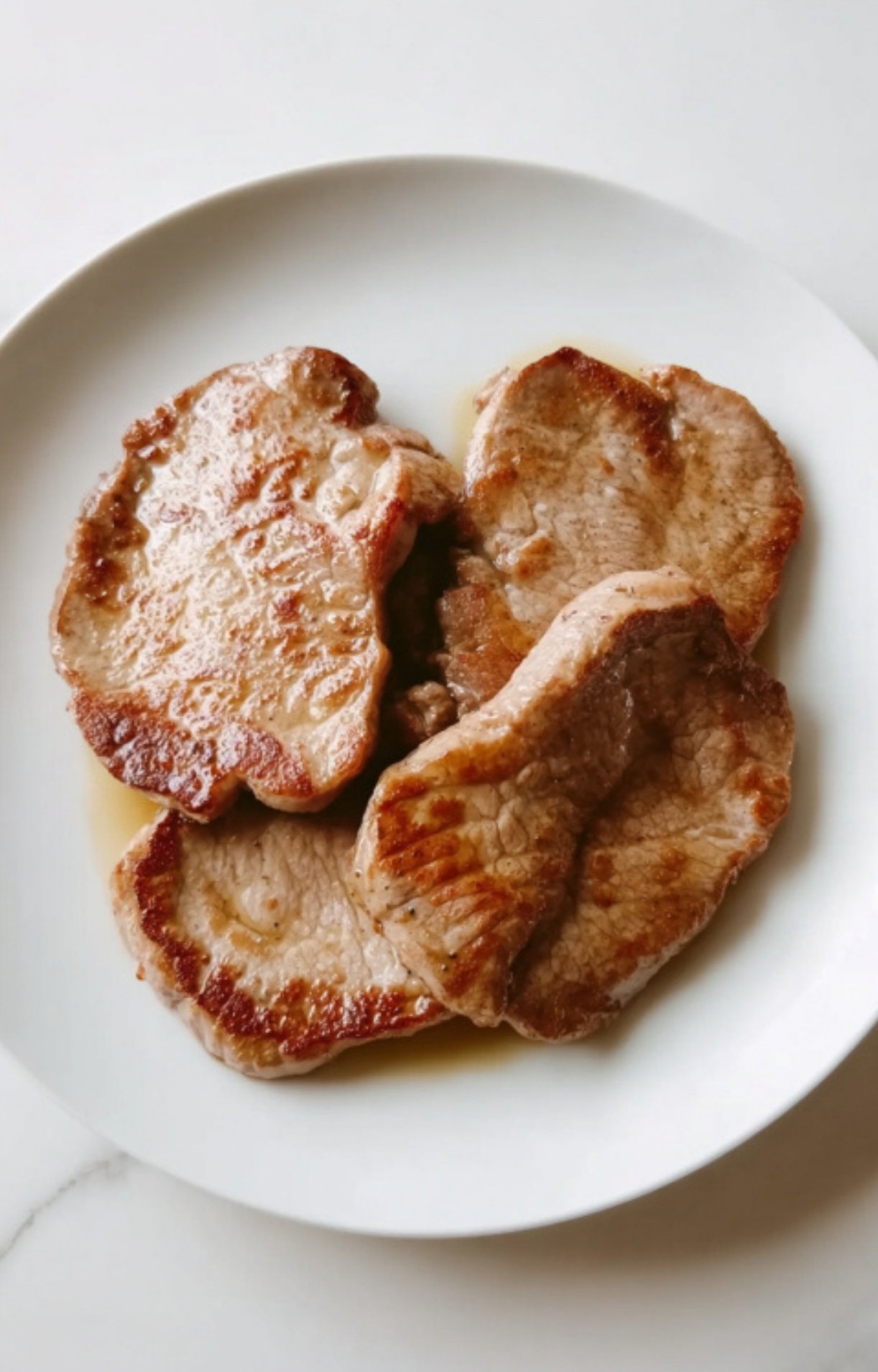 Golden brown veal cutlets resting on a white plate after pan-searing, ready for sauce