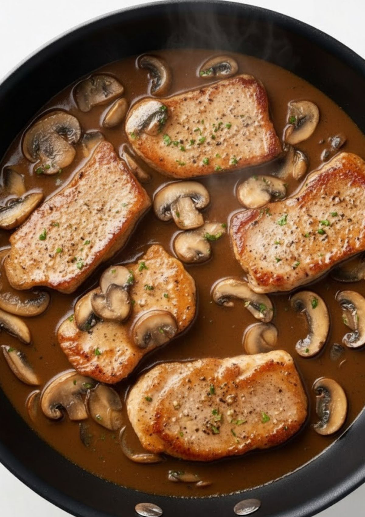 Four golden veal scallopini cutlets simmering in a creamy marsala mushroom sauce, garnished with parsley in a black skillet.