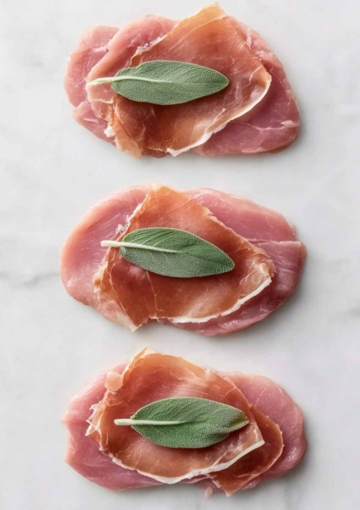 Thin slices of prosciutto and fresh sage leaves layered onto raw veal cutlets for saltimbocca style.