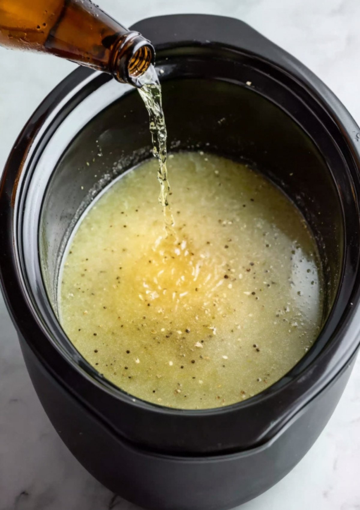 A bottle of light beer poured into a slow cooker with seasoned broth, making the corned beef extra flavorful and tender for traditional Irish meals.