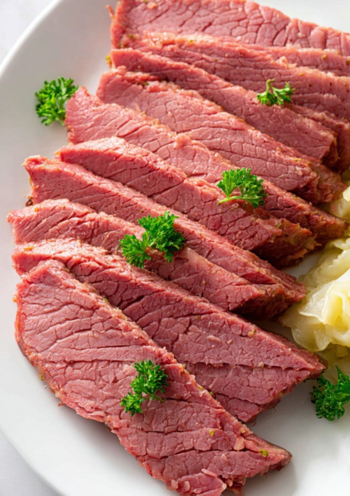 Tender slices of cooked corned beef on a white plate, garnished with fresh parsley and served with cabbage