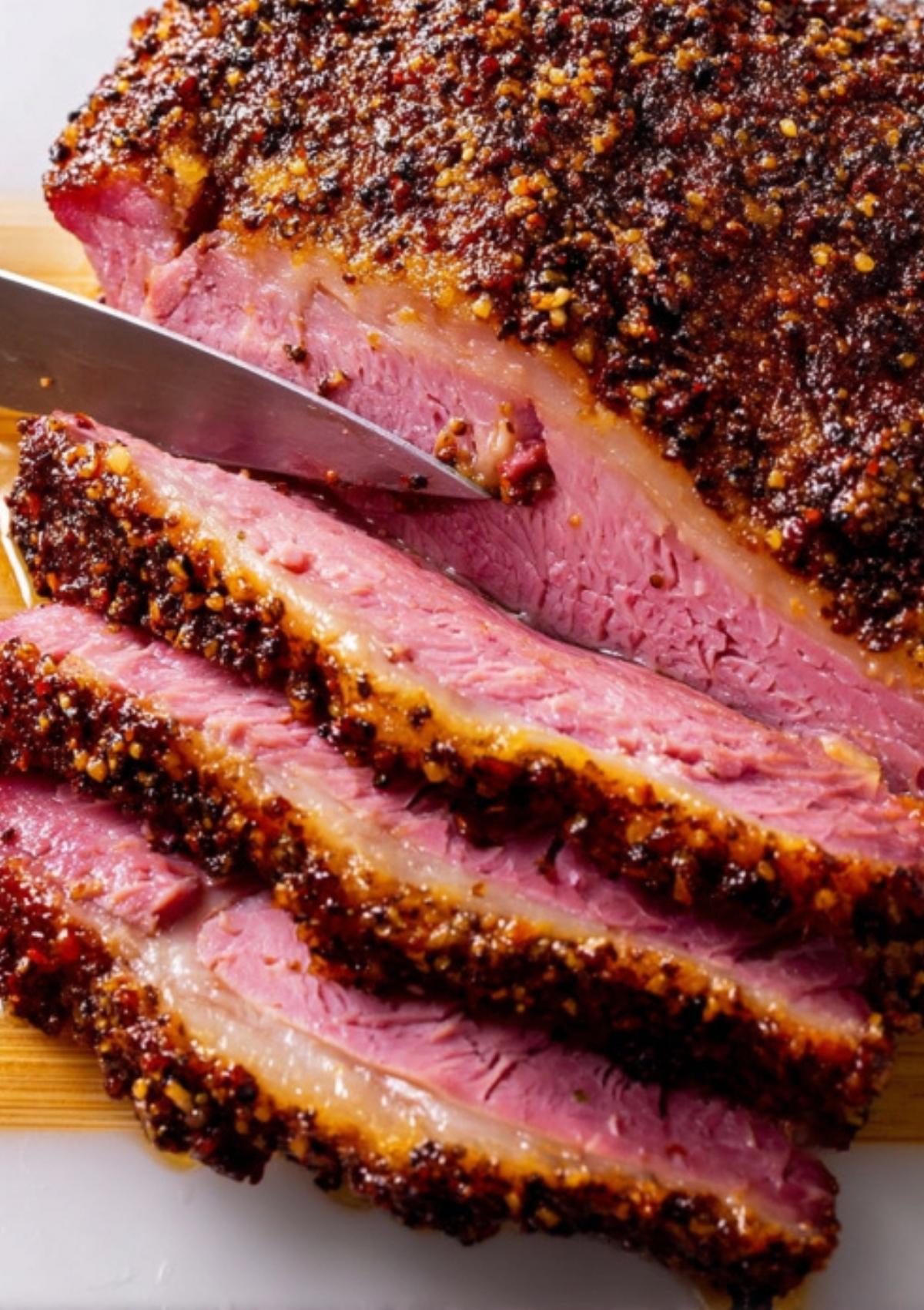 A knife slicing through a tender corned beef brisket, showing a juicy, seasoned crust and pink meat inside.