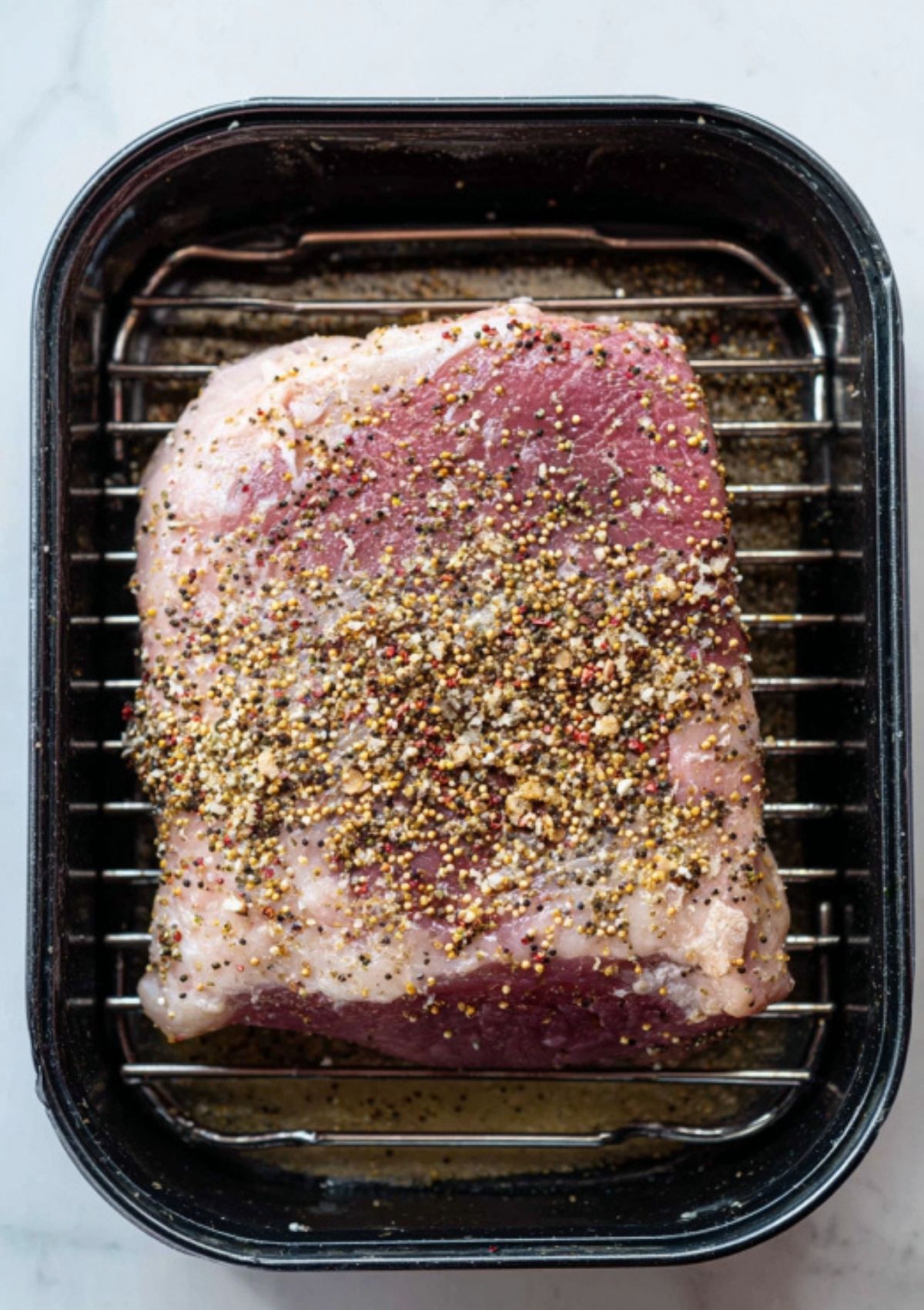 Flat cut corned beef brisket seasoned and ready on a rack in a roasting pan, showing the first step for baking this classic holiday beef recipe.