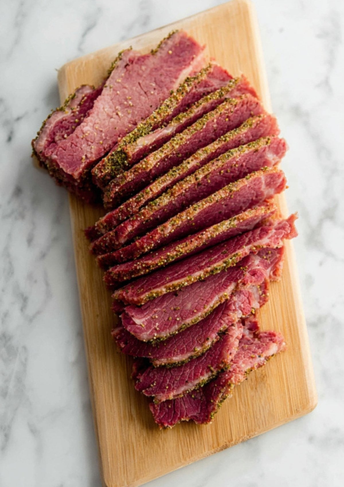 Sliced corned beef brisket arranged on a wooden cutting board. Learn the best way to slice for maximum tenderness, ideal for serving at St. Patrick’s Day or family dinners.