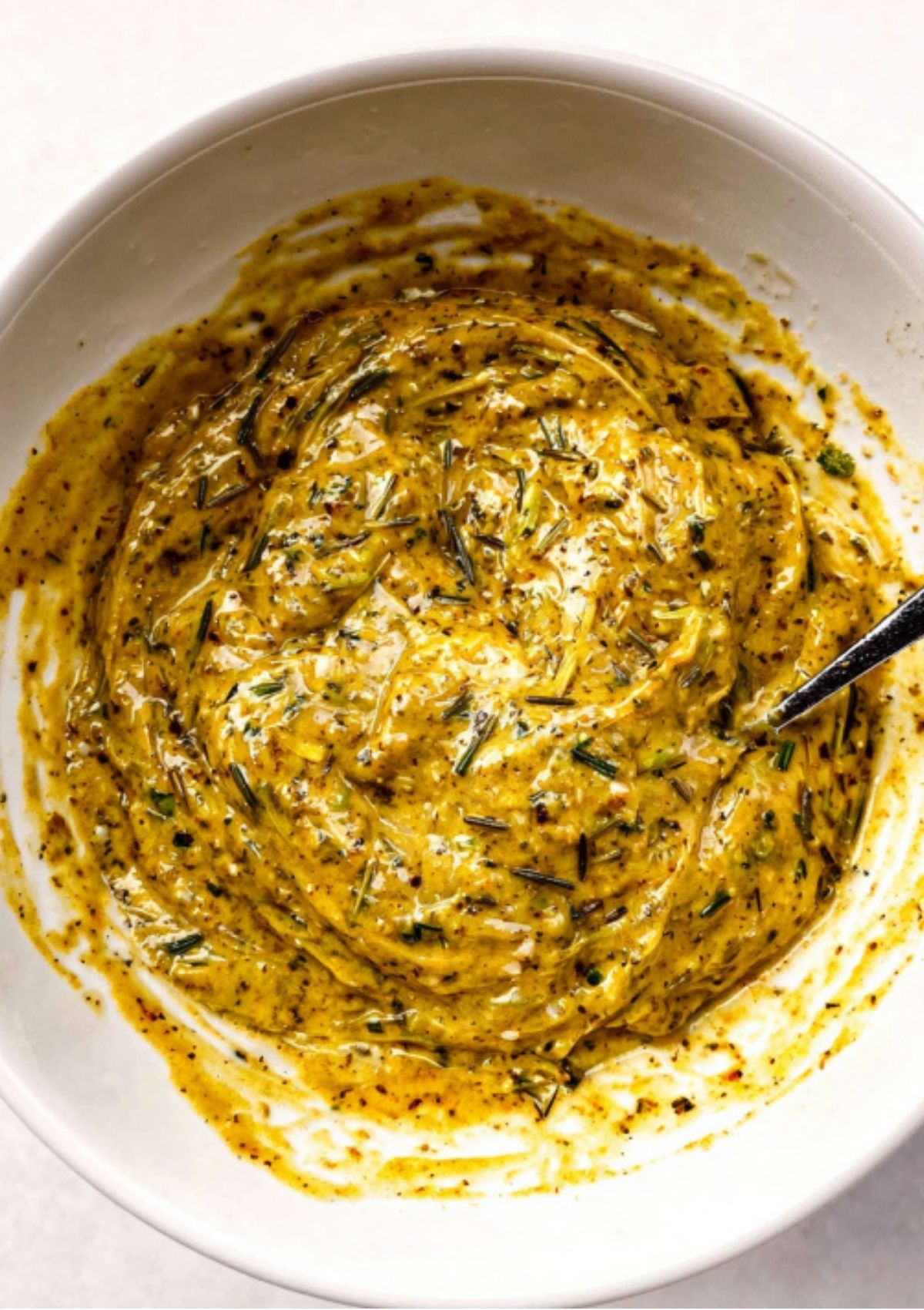Mixing bowl filled with thick garlic herb mustard marinade ready to spread on leg of lamb.