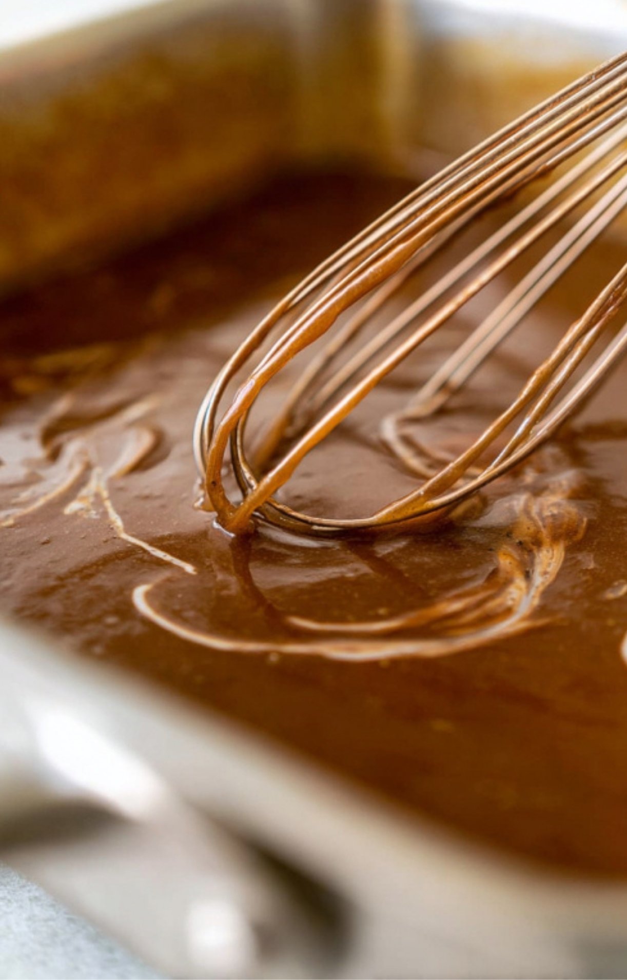Closeup of brown lamb gravy being whisked in pan, silky smooth and ready to pour over roasted lamb