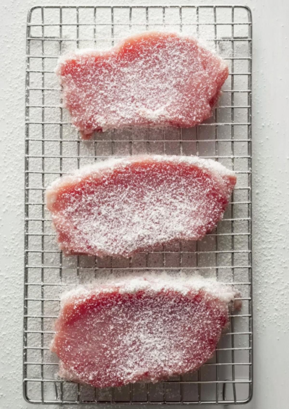 Three veal cutlets lightly coated in white flour on a wire cooling rack to ensure a crispy sear.