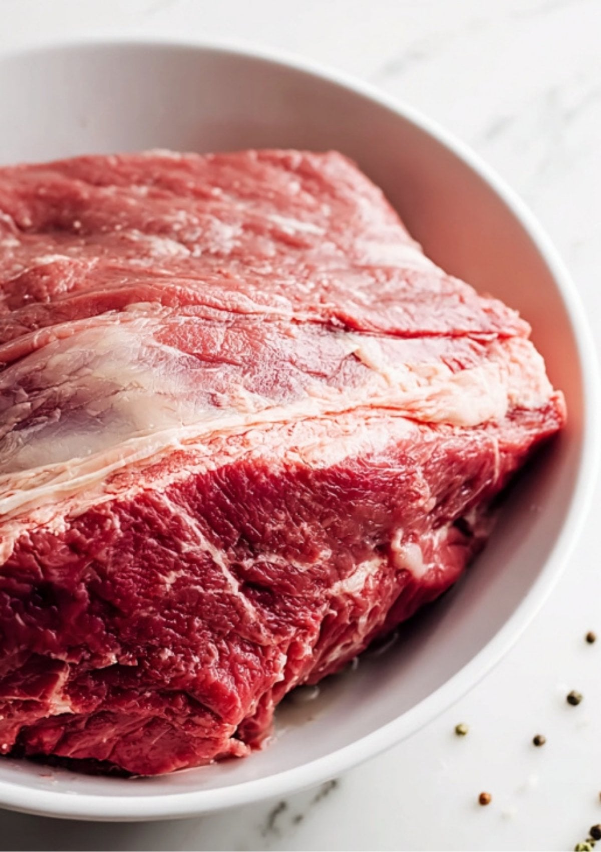 A close-up of a raw, high-quality beef brisket in a white bowl, the star ingredient for Instant Pot Corned Beef.