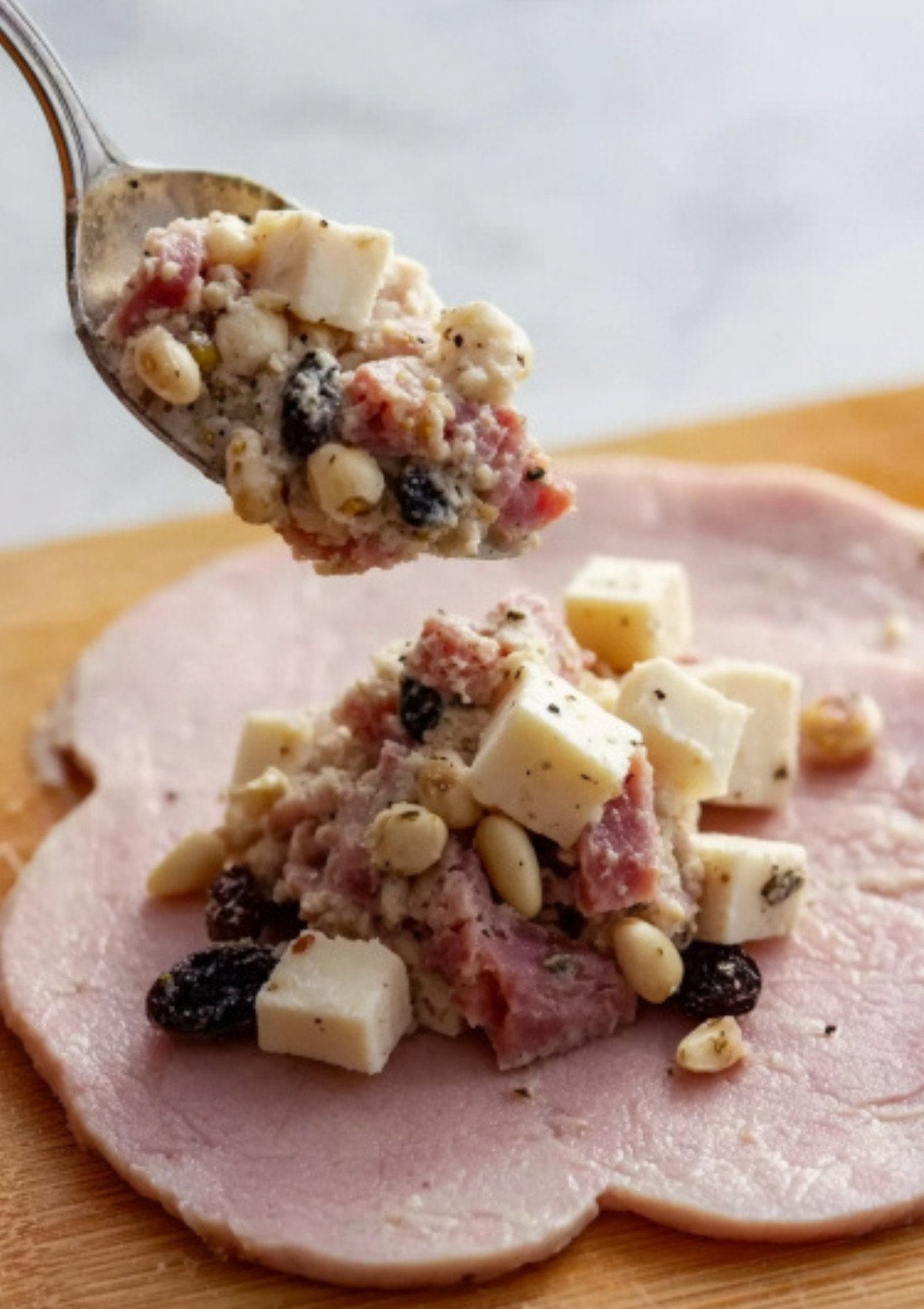 Spoonful of braciole stuffing with cubed cheese, pine nuts, and chopped meat being placed onto a thin slice of beef.