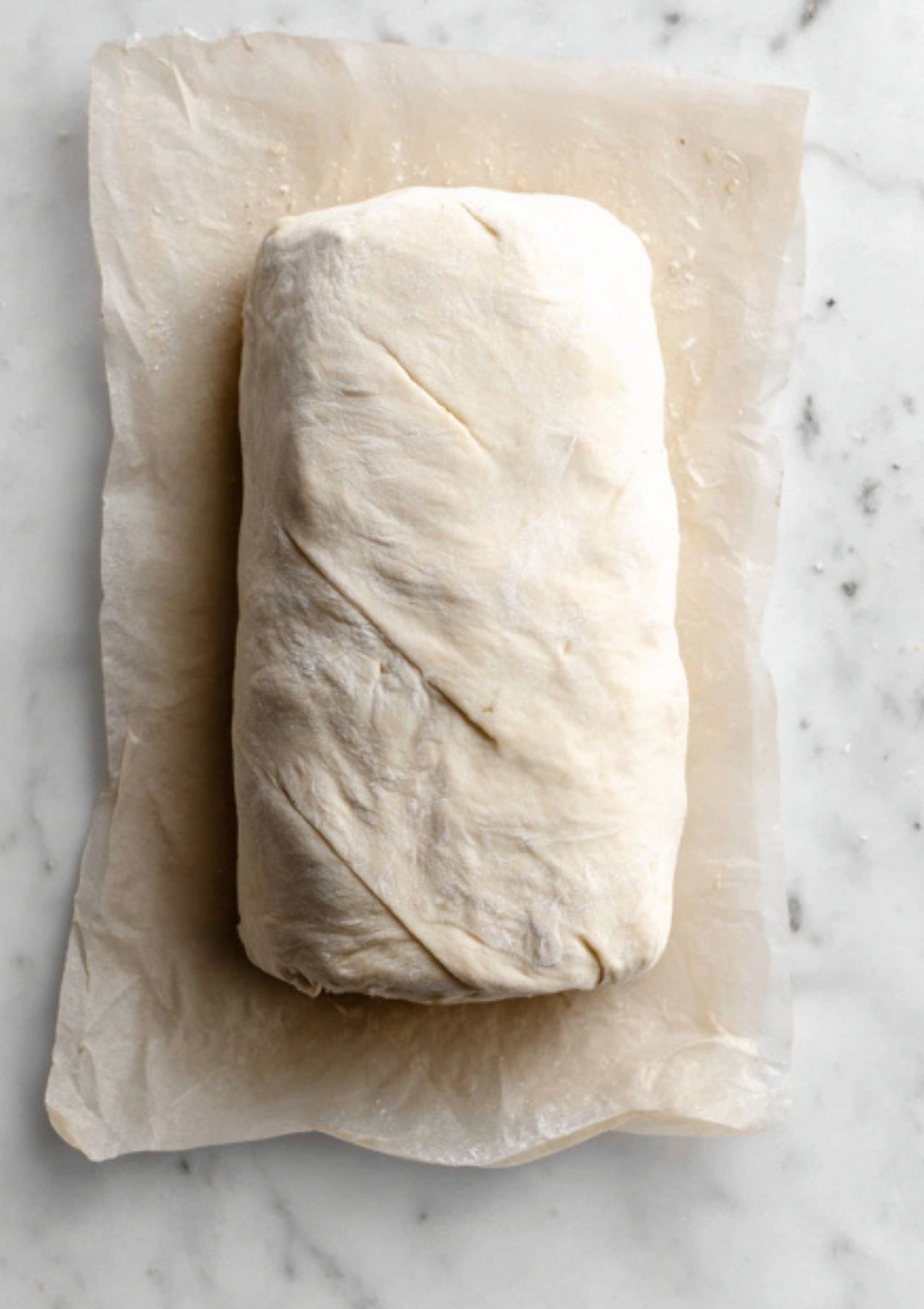 Unbaked vegan beef Wellington wrapped in puff pastry, resting on parchment paper, ready to bake. Perfect step in plant-based holiday recipes and vegan Christmas dinners.