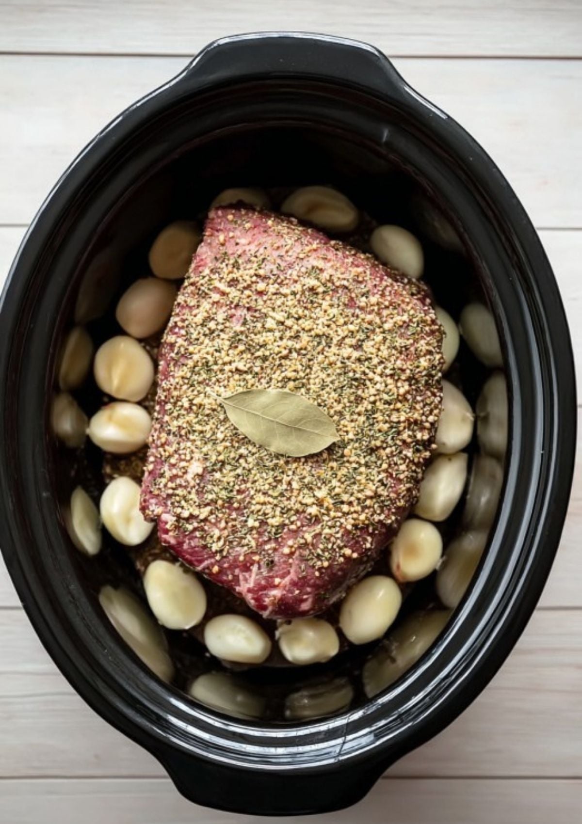 Raw corned beef brisket in a slow cooker with potatoes, coated in spices and topped with a bay leaf. Simple setup for a classic St. Patrick’s Day meal or weeknight comfort food.