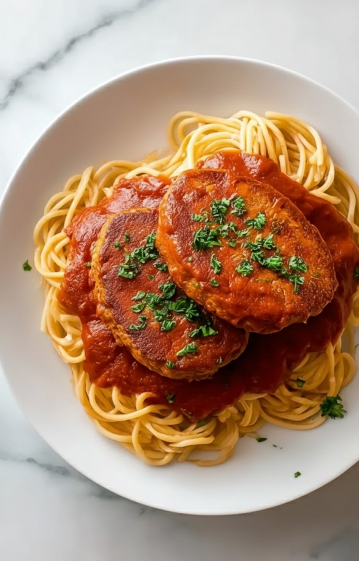 Overhead view of a white plate with spaghetti and two veal cutlets covered in tomato sauce and parsley. Homemade Italian comfort food for any night.