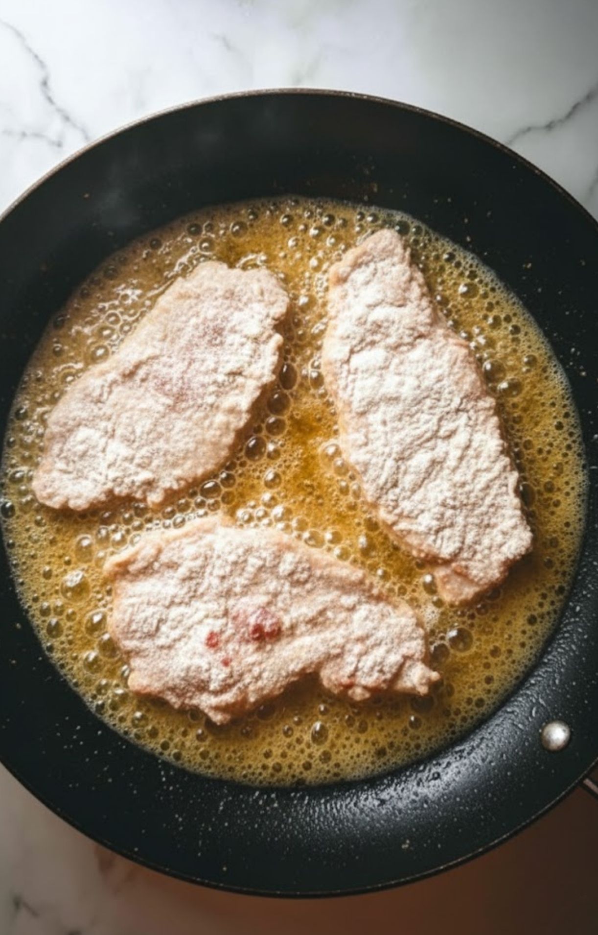 Three flour-coated veal cutlets frying in a bubbling skillet, the start of a classic Italian veal piccata in white wine sauce. Best for quick weeknight meals and family dinners.