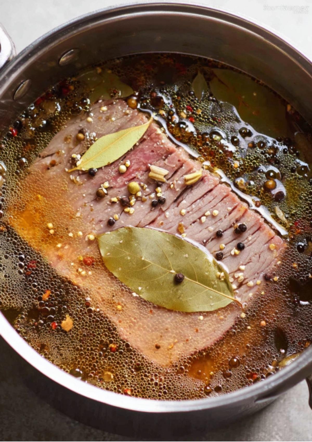 Beef brisket simmering in a pot of water with bay leaves, peppercorns, and spices as it cooks to tender perfection for classic corned beef.