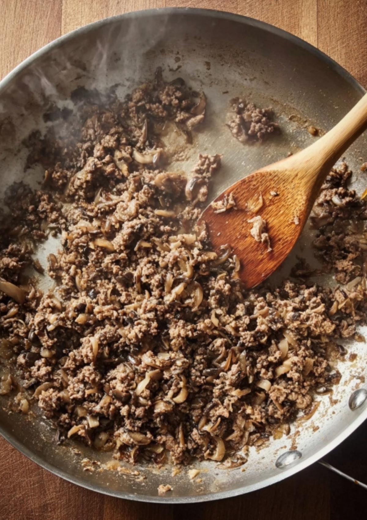 Savory mushroom duxelles sautéed in a pan, a key layer in beef Wellington puff pastry, bringing rich umami flavor to this holiday dinner favorite.