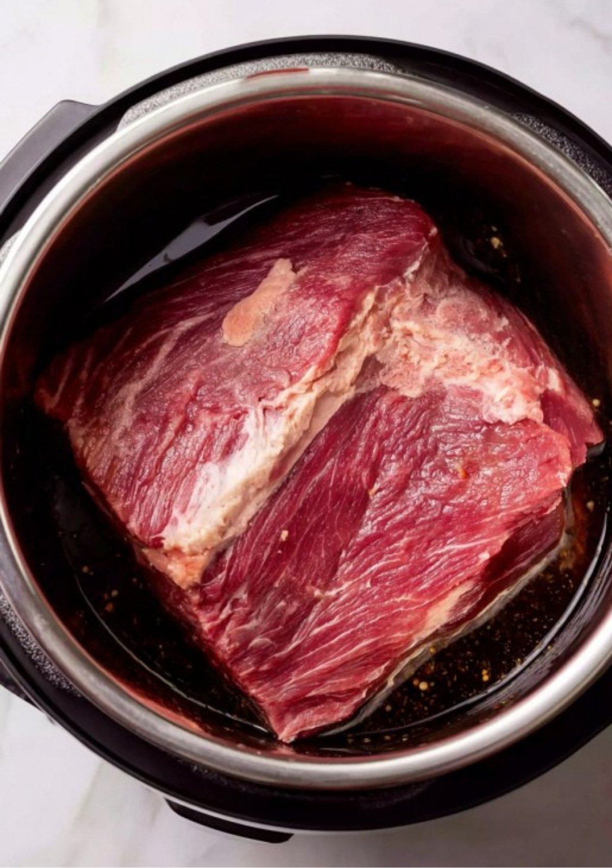 A large beef brisket placed inside the stainless steel inner pot to begin the pressure cooking process for Instant Pot Corned Beef.