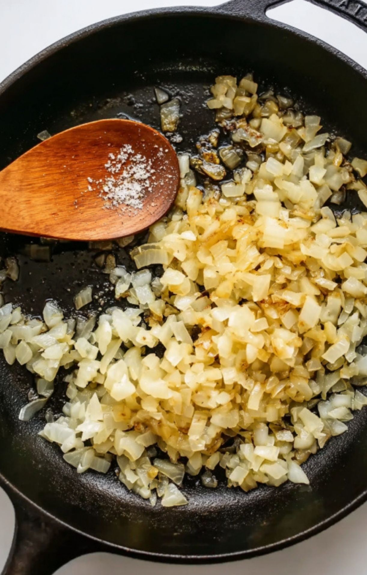 Diced onions sautéing in a cast iron skillet with a wooden spoon, ready to be added to corned beef hash.