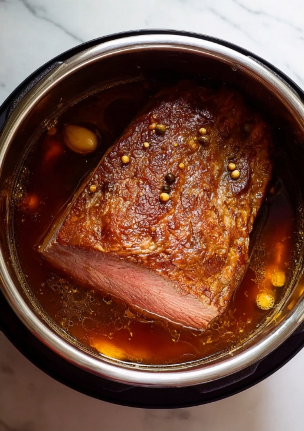 The beef brisket submerged in a rich, spiced braising liquid inside the pot, halfway through the Instant Pot Corned Beef cooking cycle.