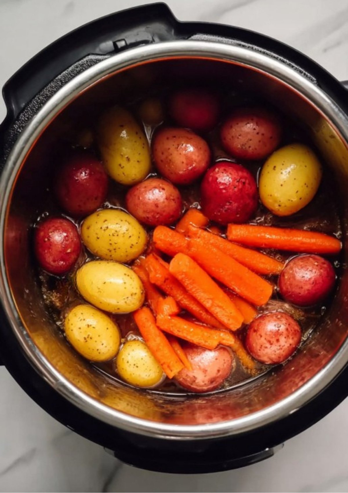 Whole red and yellow baby potatoes and carrot sticks steaming in the seasoned broth after the Instant Pot Corned Beef has been cooked.